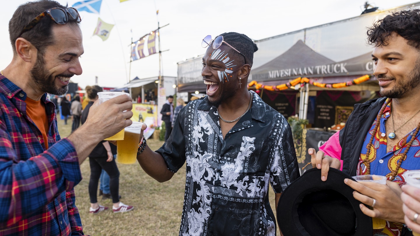 Group of mixed age and ethnic male friends having fun at a festival in Northumberland, North East England. They are laughing and drinking beer together, toasting their pints.
1457658884