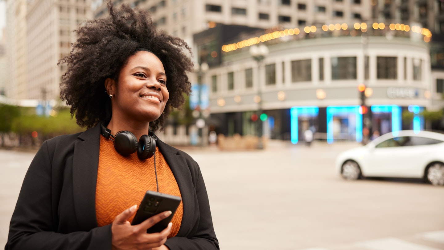 Immersed in the urban rhythm, a woman in a suit and headphones stands in downtown Chicago, awaiting her carpool with poised anticipation.
1498638733
A woman smiling on the side of the street in Chicago