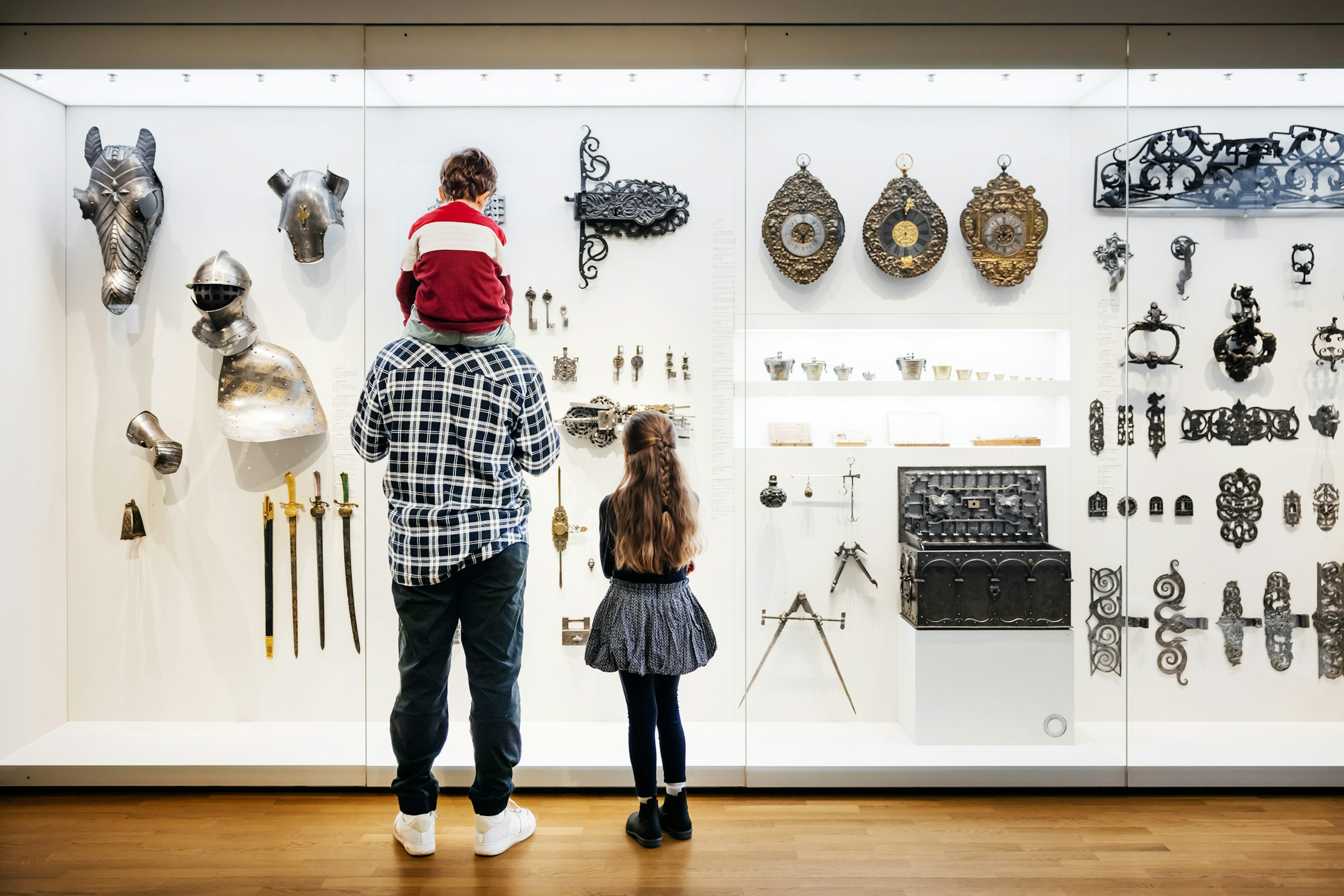 A single dad standing next to his daughter and carrying his son on his shoulders while looking at an exhibit in a  museum together.