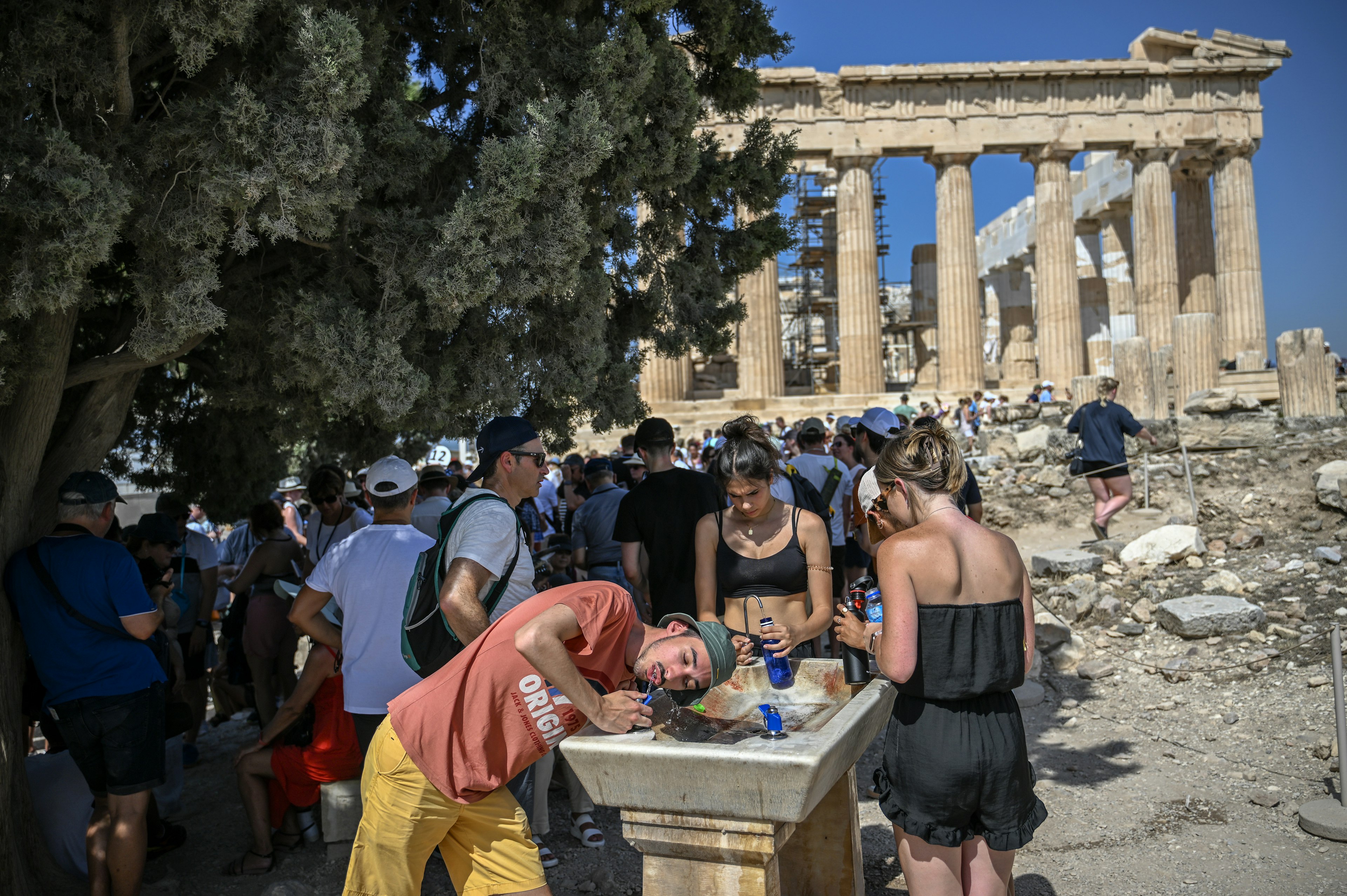 Tourists cool off at a water fountain during their visit to the Parthenon Temple on the Acropolis Hill