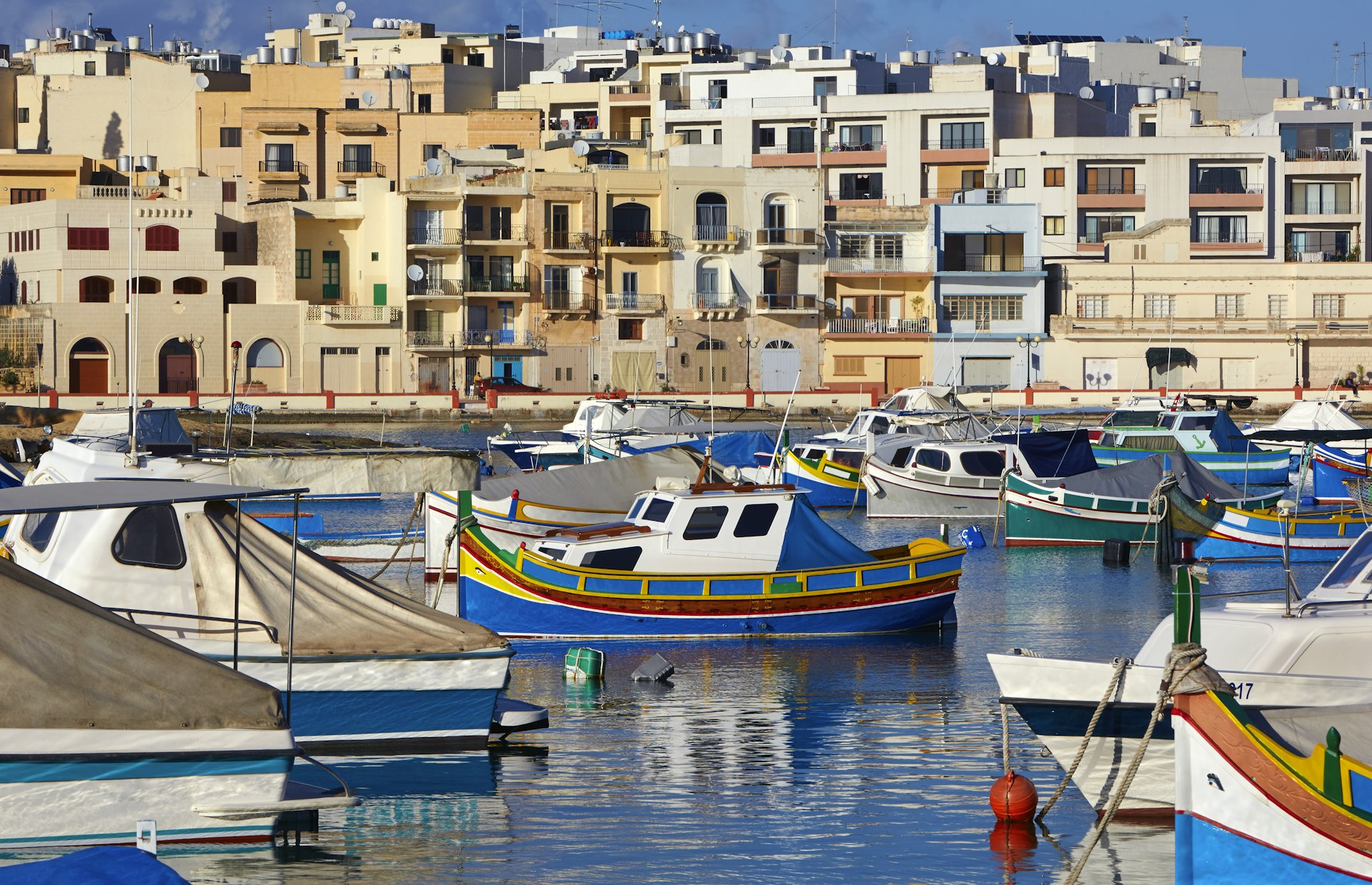 Traditional colourful Maltese fishing boats with traditional Maltese housing in St George's Bay