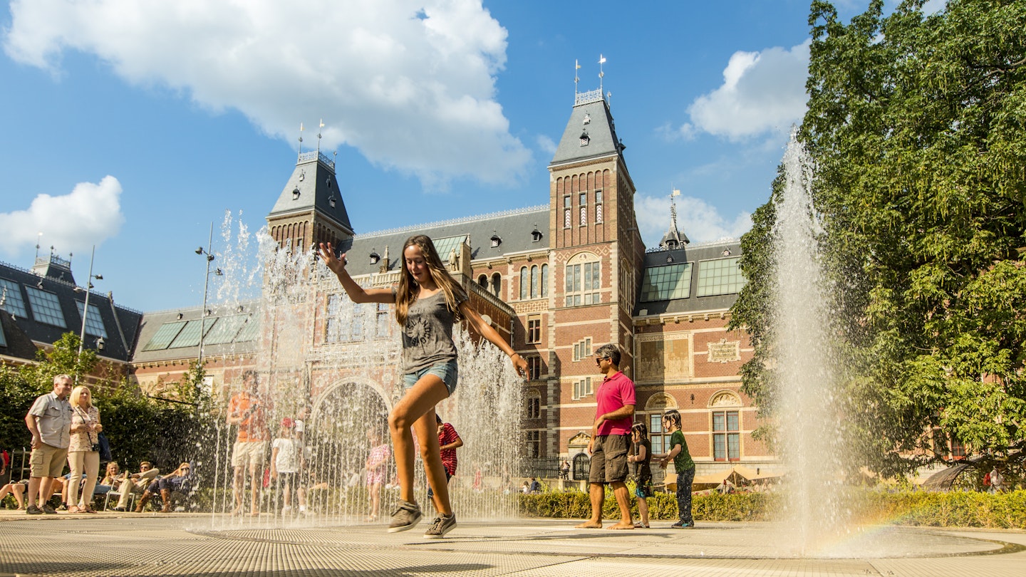 Families and tourists relax in the garden of the Rijksmuseum, the fountain forms an attraction in itself, inviting the old and young to interact with it, occassionaly resulting in wet clothes. People rushing in and out of the water spray. 509788919 Carefree, Fun, Joy, Playful, Togetherness The Rijksmuseum garden with fountain - stock photo Families and tourists relax in the garden of the Rijksmuseum, the fountain forms an attraction in itself, inviting the old and young to interact with it, occassionaly resulting in wet clothes. People rushing in and out of the water spray.