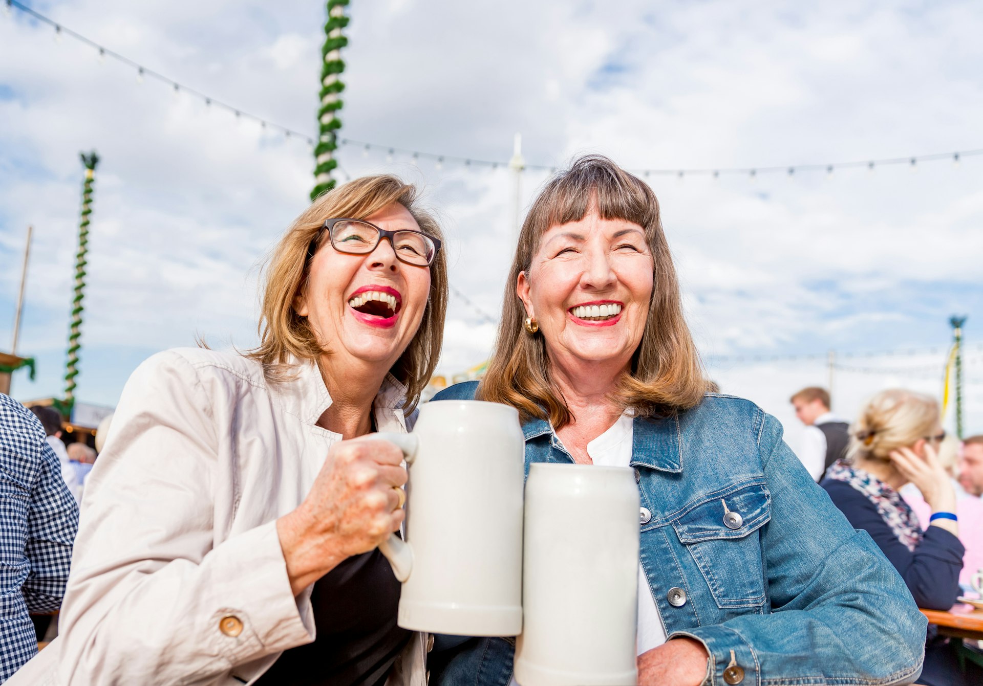 Two senior women smile as they clink their glasses together at a beer festival