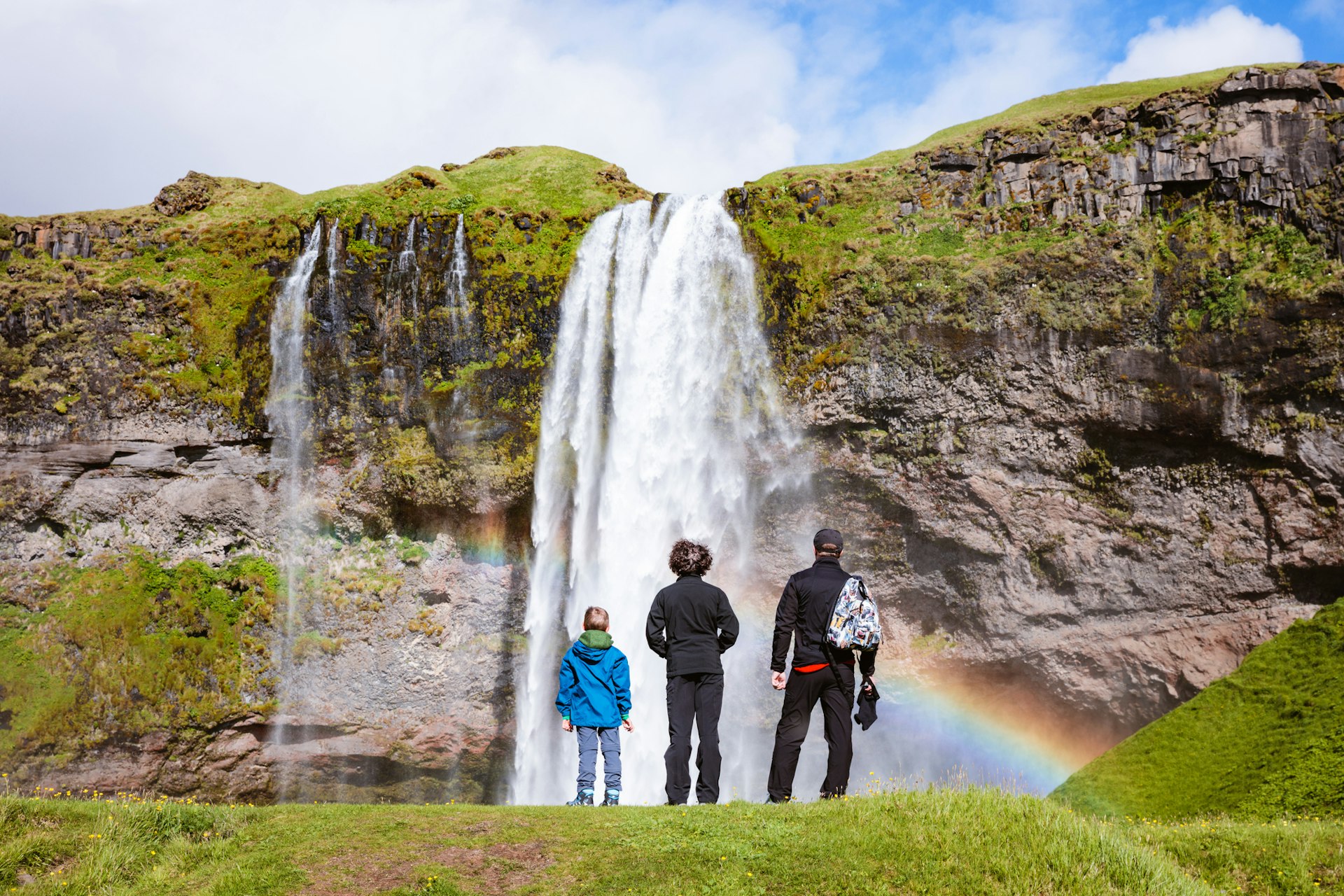 Man with children standing in front Seljalandsfoss waterfall in summer