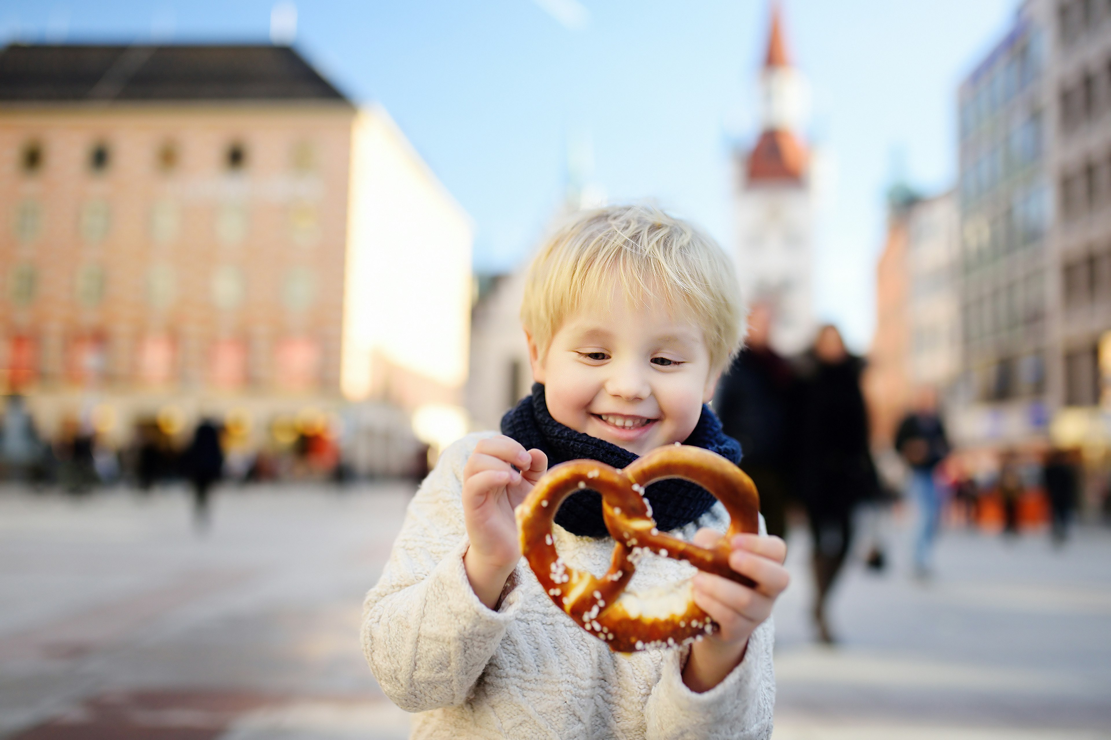 A small blonde boy looks delighted with the prezel he's holding in the centre of Munich