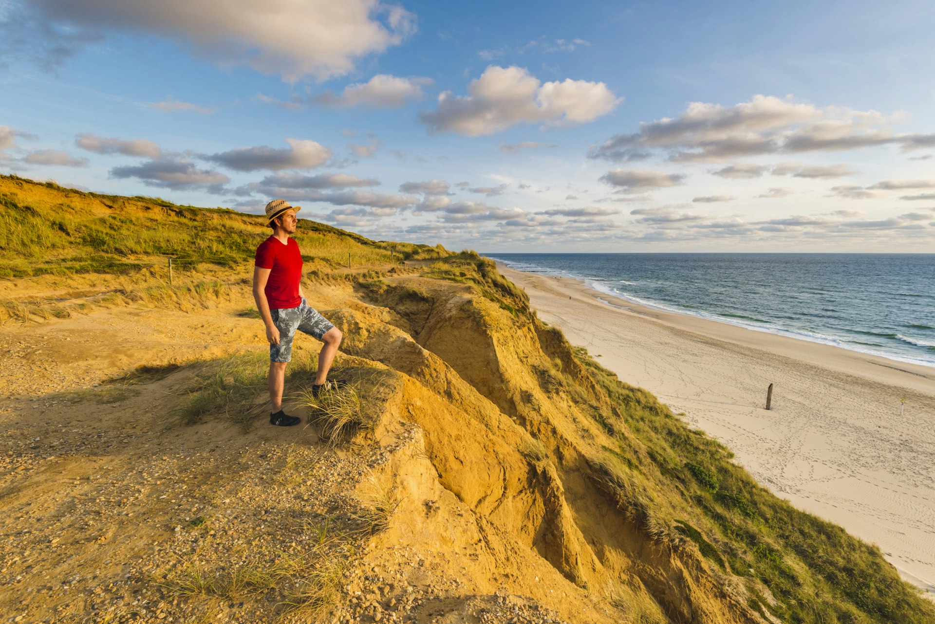 A man stands on a sandy dune and stares out over the beach towards the sea on a sunny day