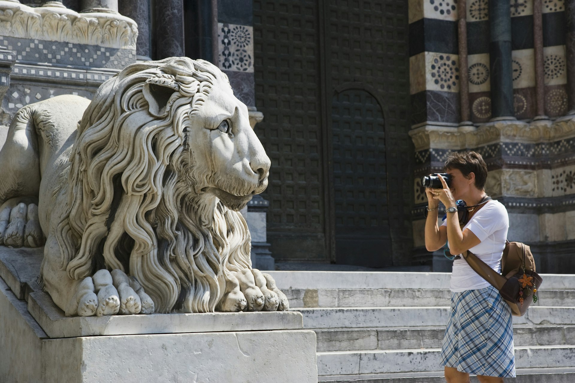 A woman taking a picture of a lion statue outside the cathedral in Genoa.