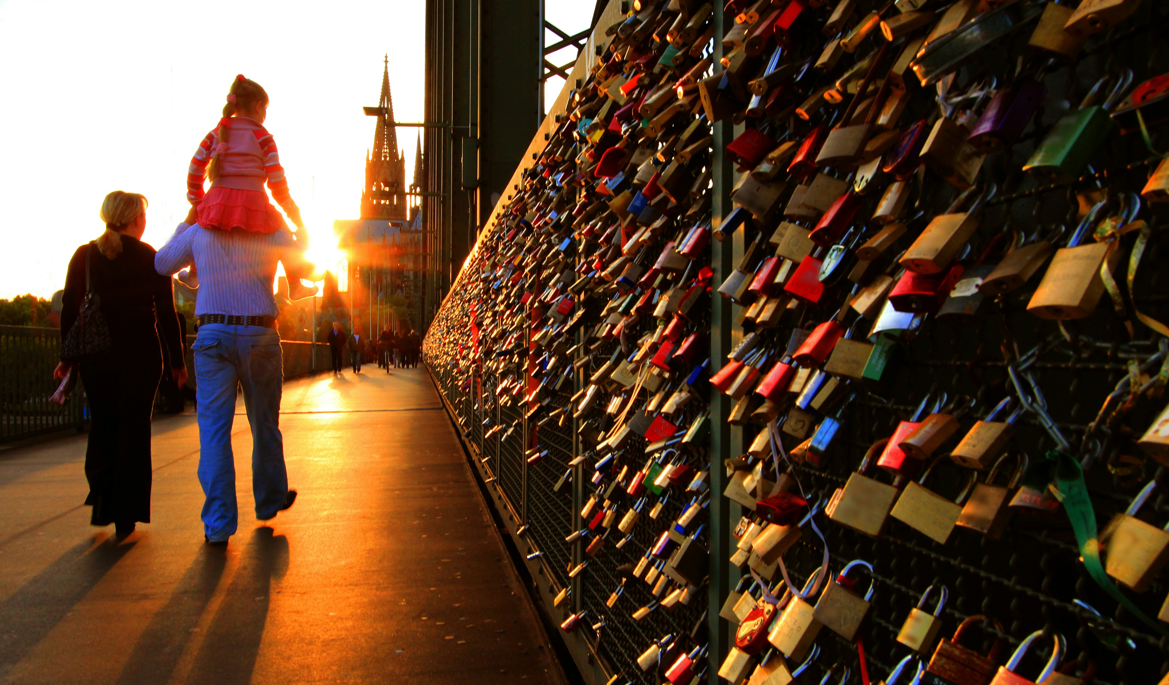 People walk past a series of padlocks attached to railings on a bridge