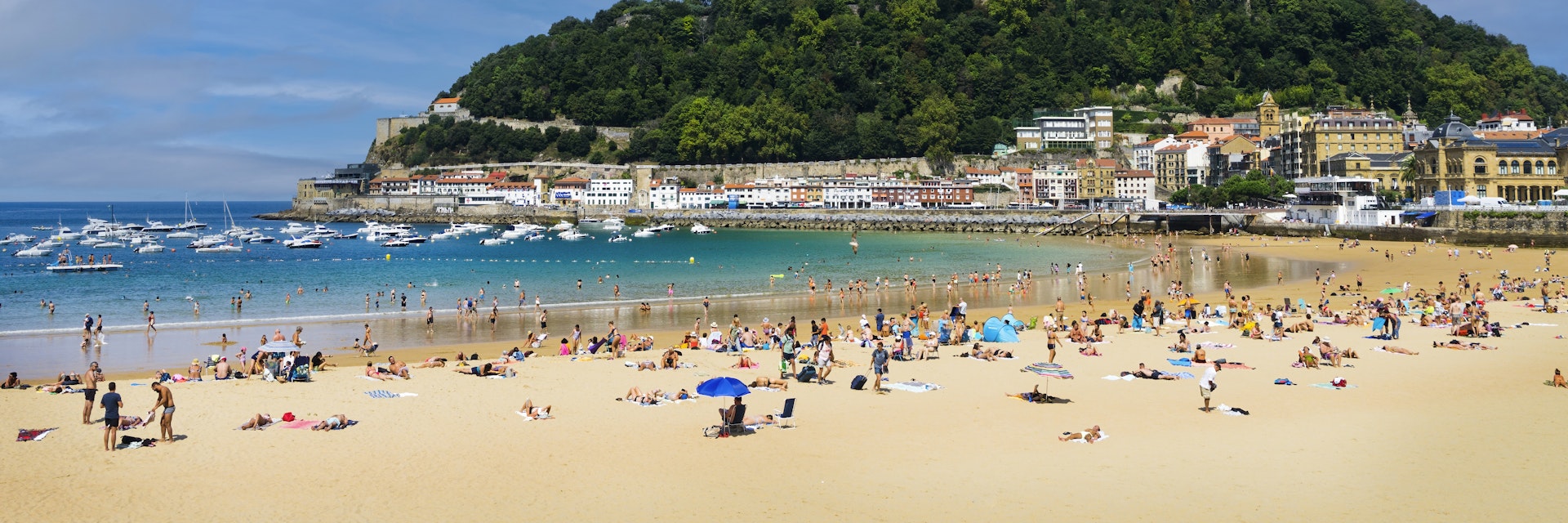 Landscape of La Concha beach in the city of San Sebastian, in the Spanish Basque Country, on a sunny day with people enjoying the beach and Mount Urgull in the background.