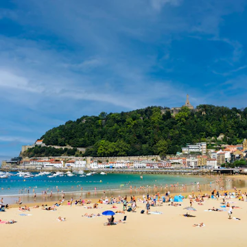 Landscape of La Concha beach in the city of San Sebastian, in the Spanish Basque Country, on a sunny day with people enjoying the beach and Mount Urgull in the background.