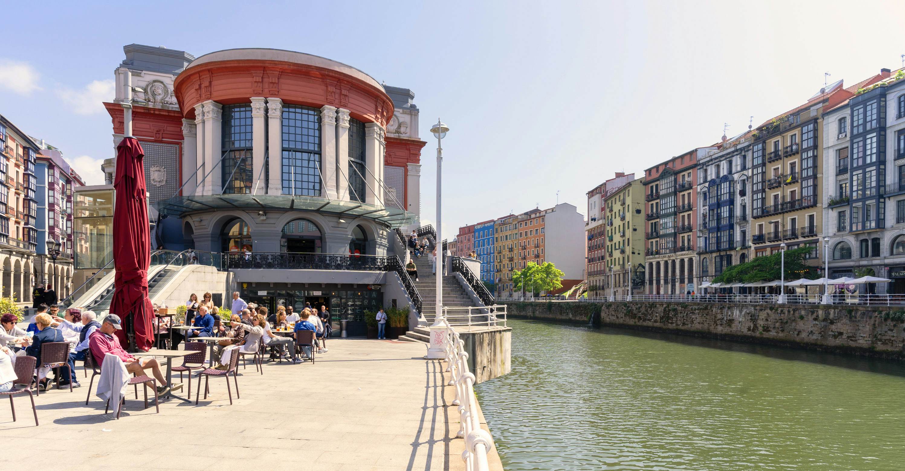 Bilbao Ribera market next to the Nervión river on a sunny day with people sitting on the terrace.