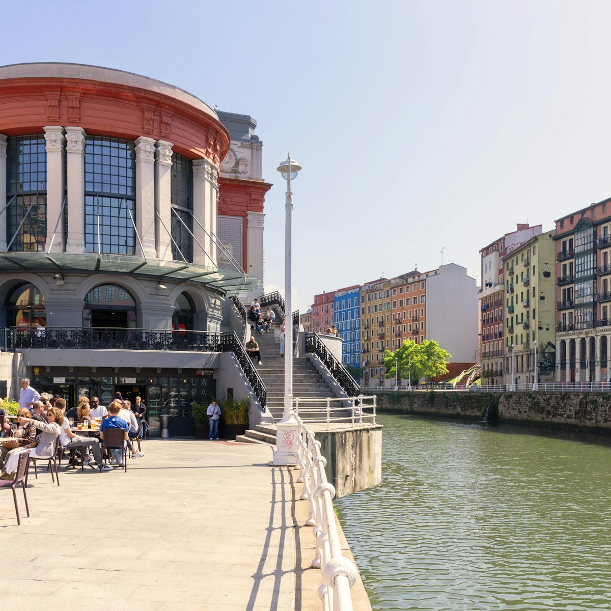 Bilbao, Spain. Bilbao Ribera market next to the Nervión river on a sunny day with people sitting on the terrace.