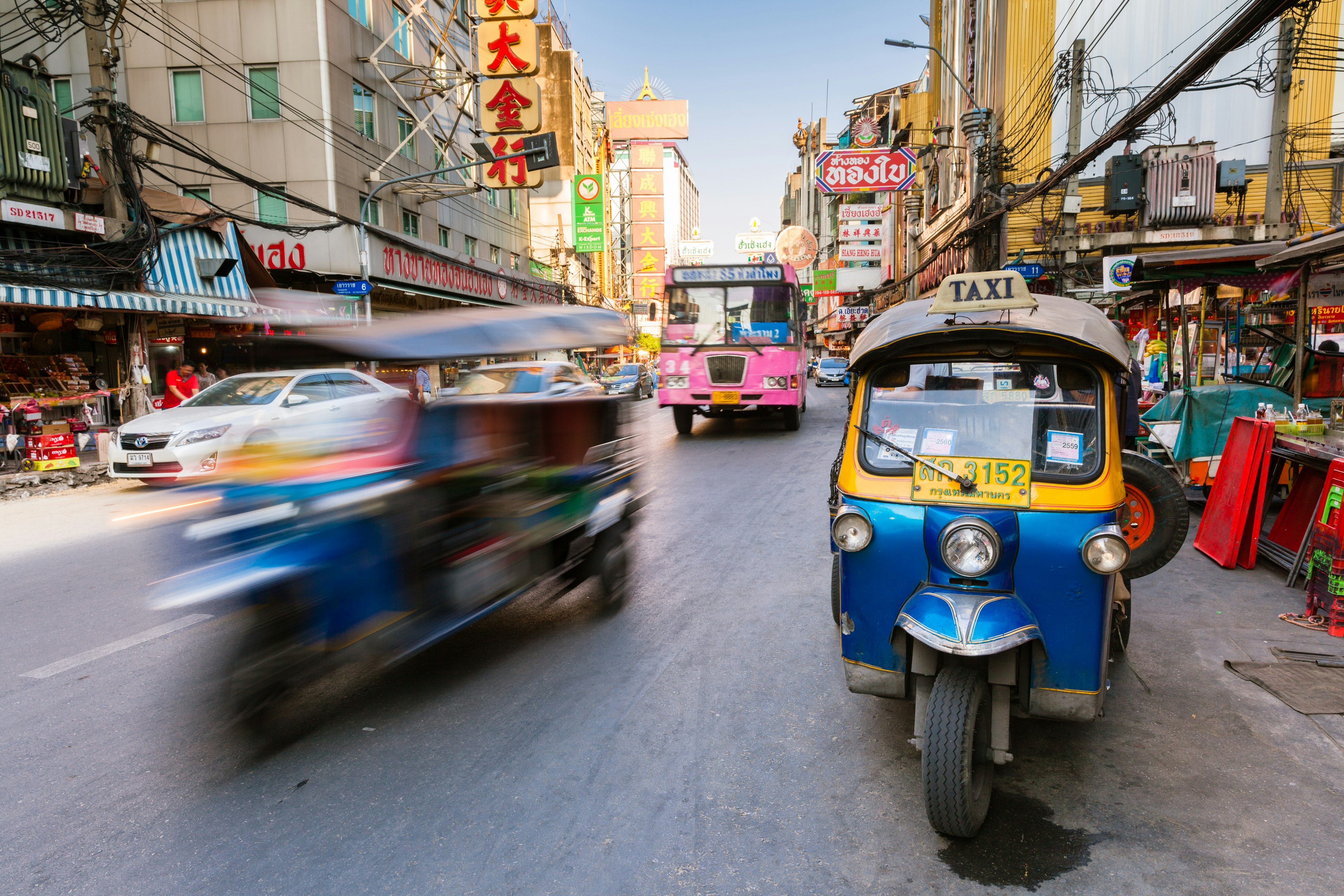 A small motorized rickshaw parked on a busy street as a bus and car pass by