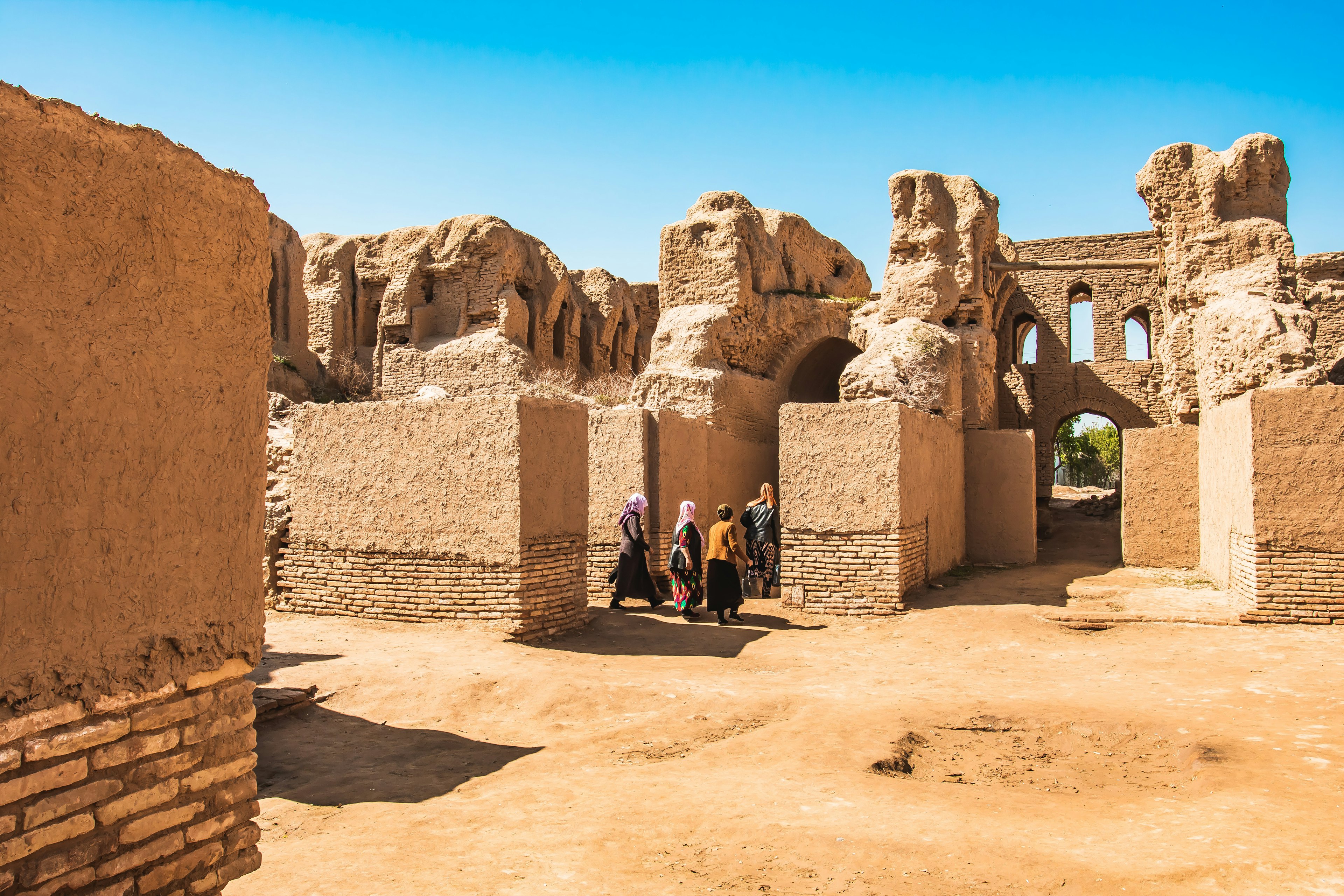 People tour their way through a ruined structure with walls made of red mud