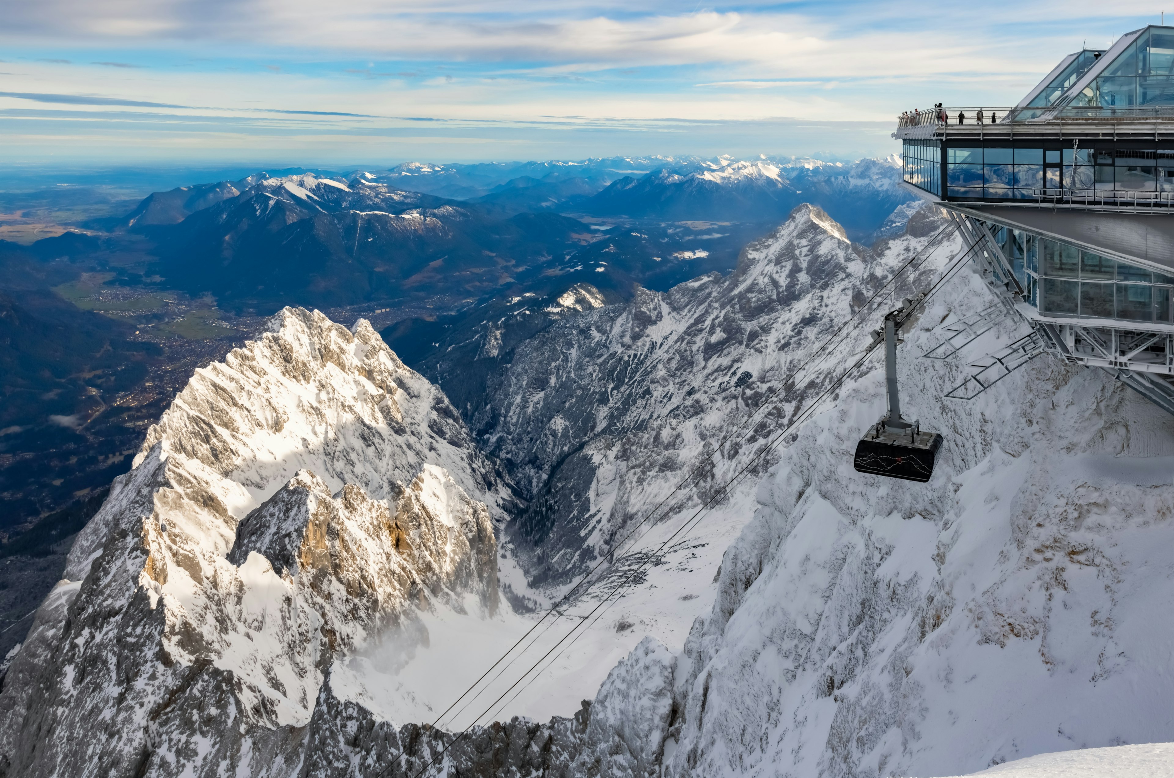 A cable car station with viewpoint pearched at the top of a mountain with snowy peaks stretching into the distance