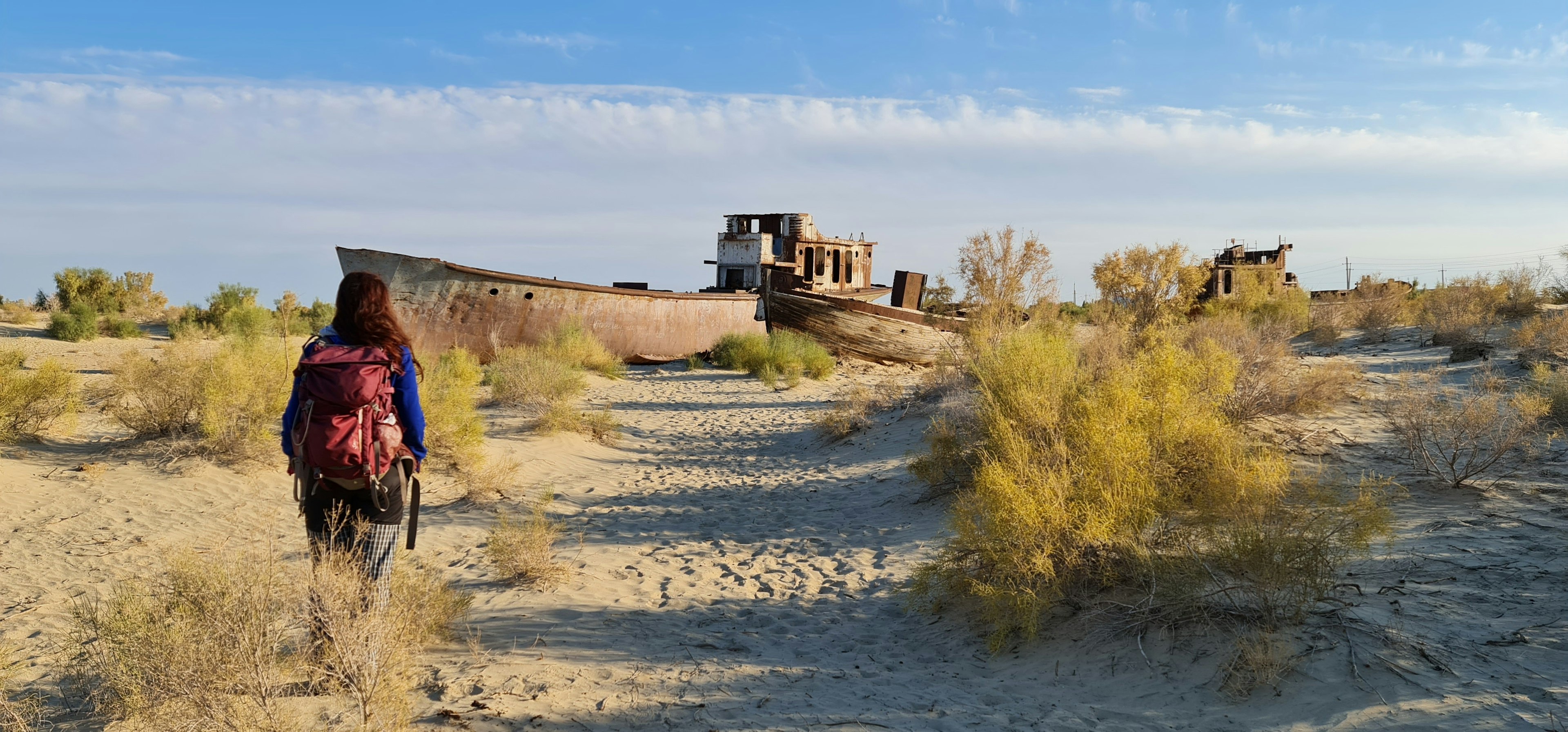 A woman walks among stranded fishing trawlers and boats on the sandy dry ground that was once the bottom of the Aral Sea