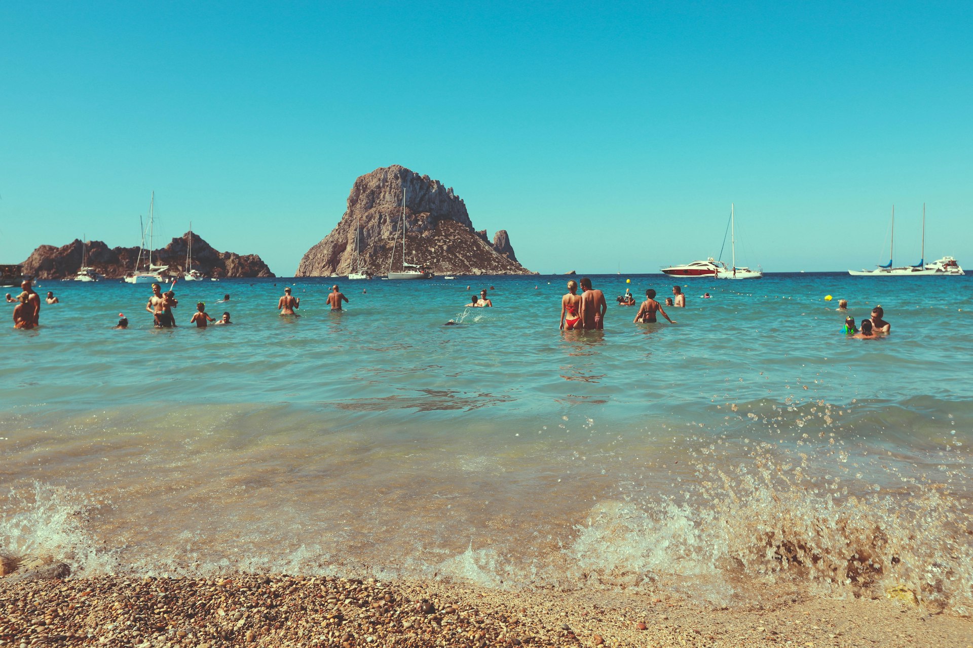 Swimmers in the water at Cala d’Hort beach with Es Vedrà island in the distance, Ibiza, Spain