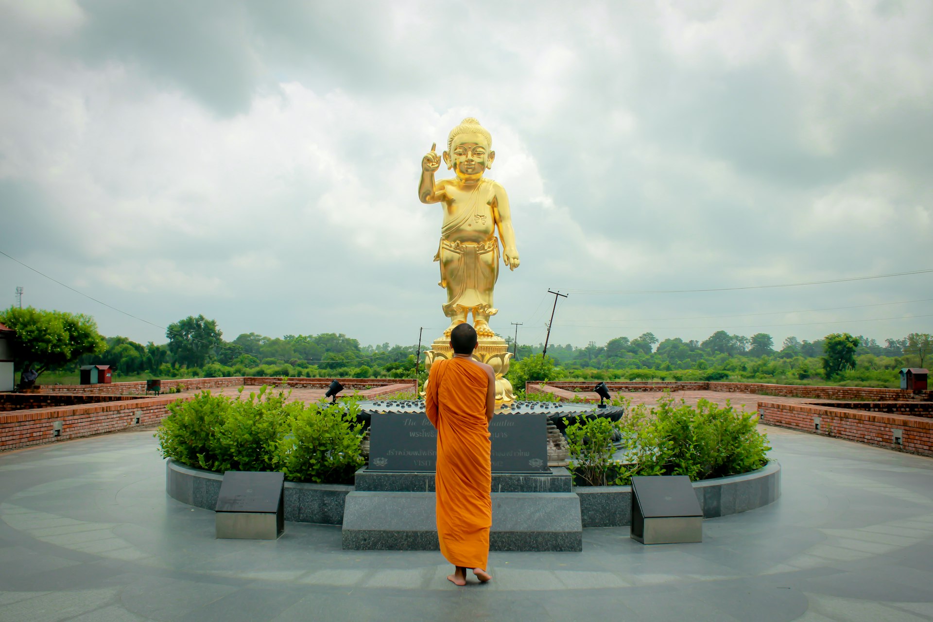 A monk in orange robes stands in front of a gold buddha statue