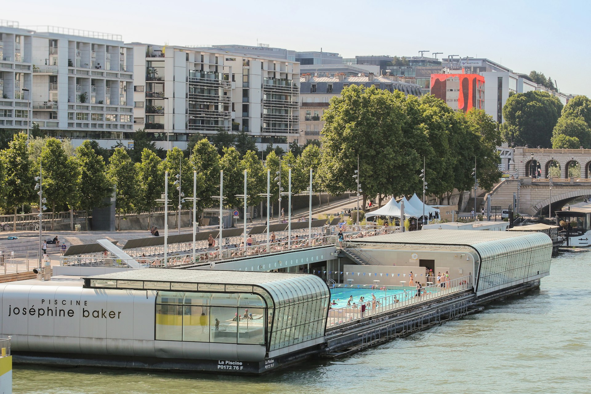 An open-air swimming pool complex floating on the edge of a river