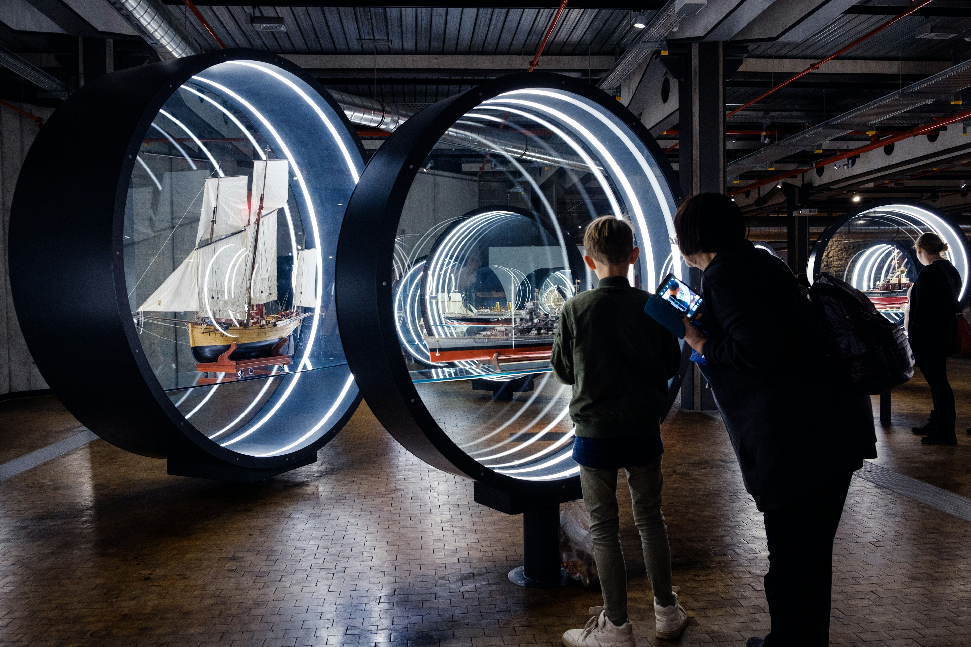 An adult and a child peer at an interactive boat exhibition in a museum