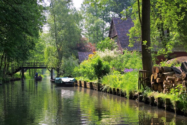 A boat floating past a wood-framed house on a greenery-lined canal in the Spreewald region of Germany