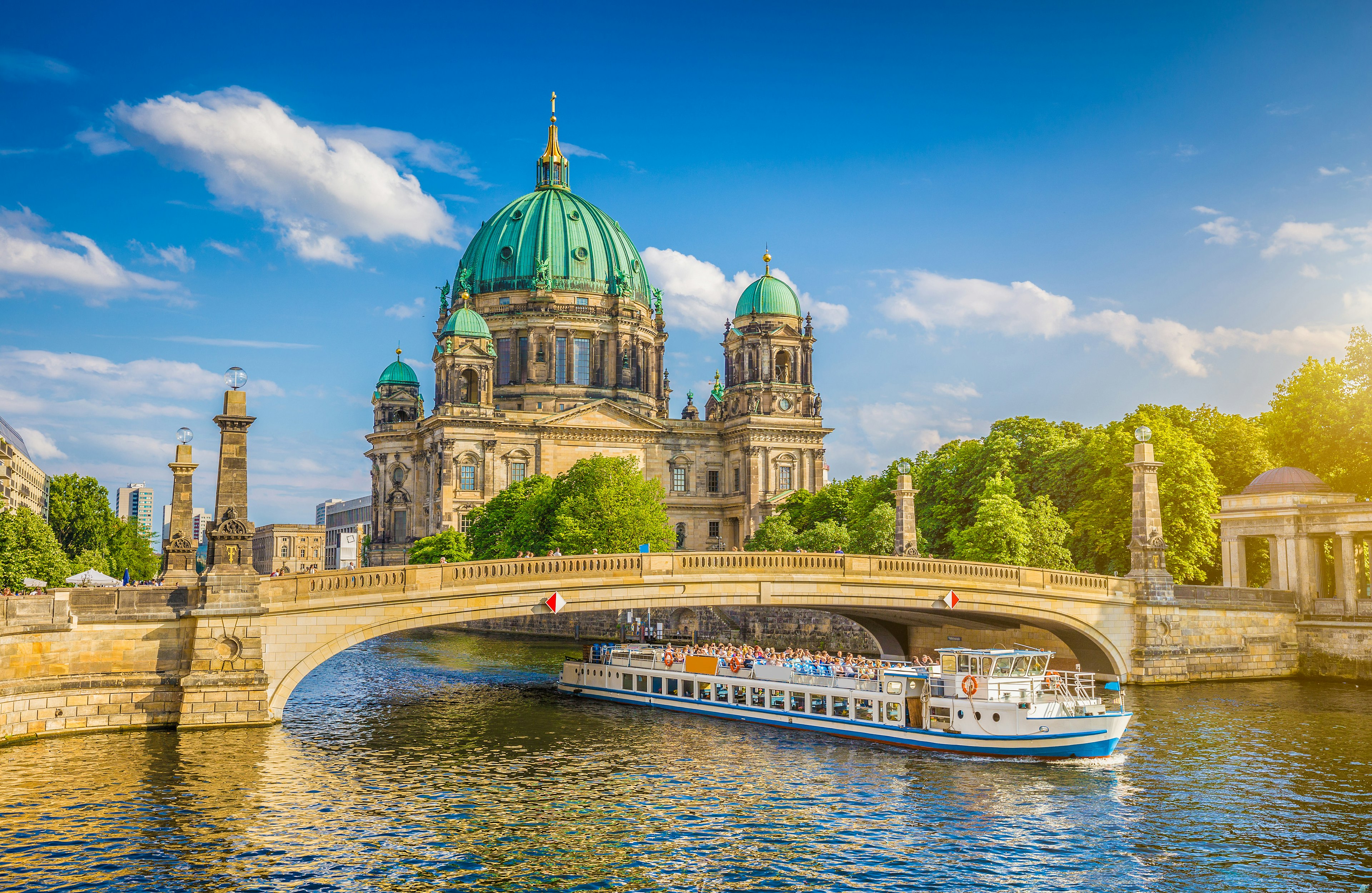 A boat laden with passengers travels along a river next to a large domed cathedral