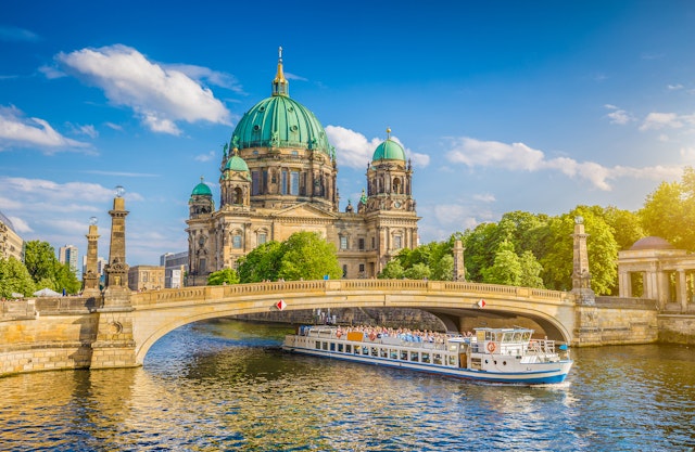 A boat laden with passengers travels along a river next to a large domed cathedral