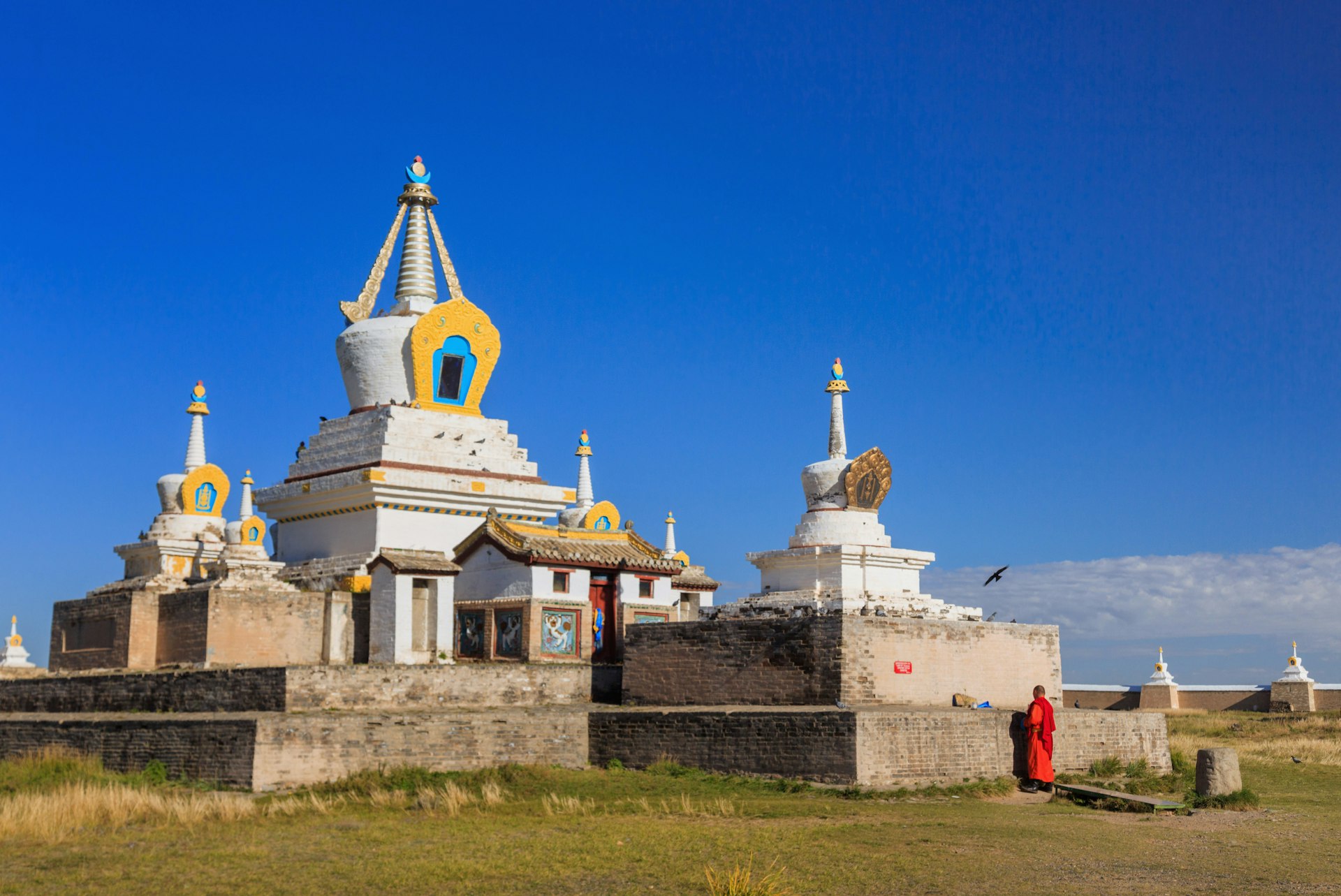 A Buddhist monk in red robes stands before a stupa