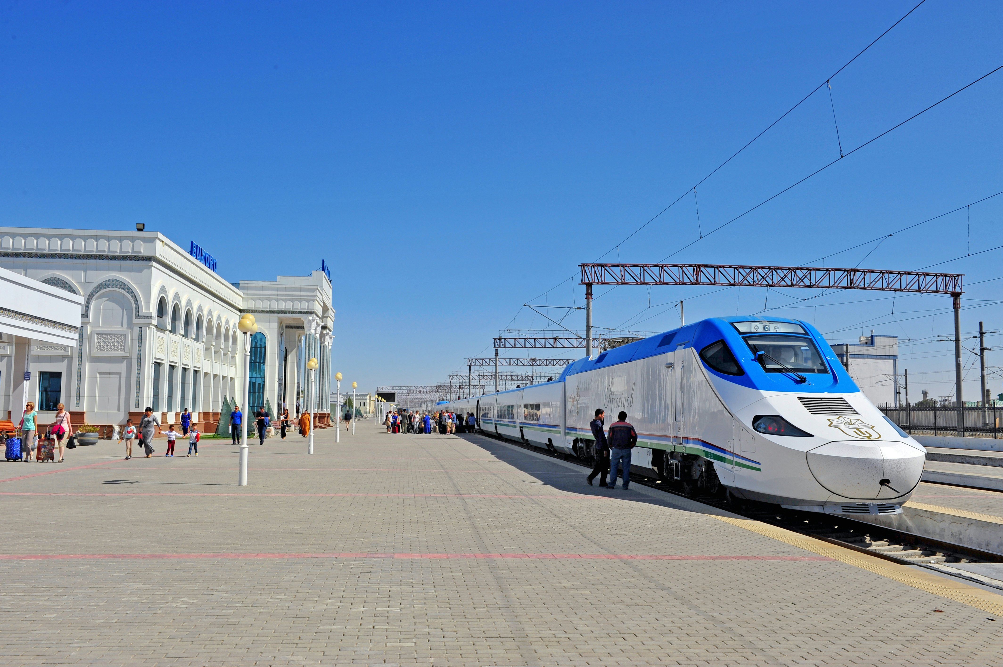 A white train with a blue roof stands at a station as people board