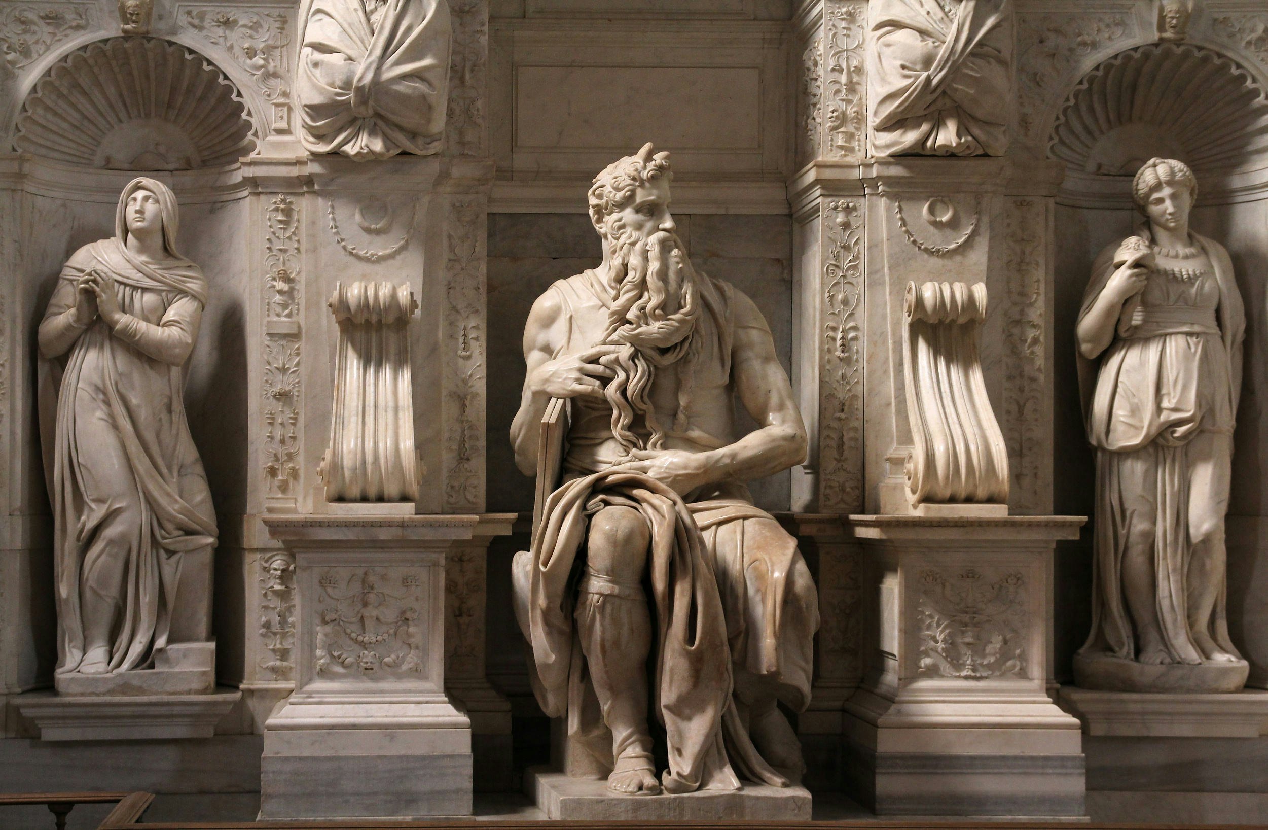 A marble statue of a seated man with a large beard and horns.