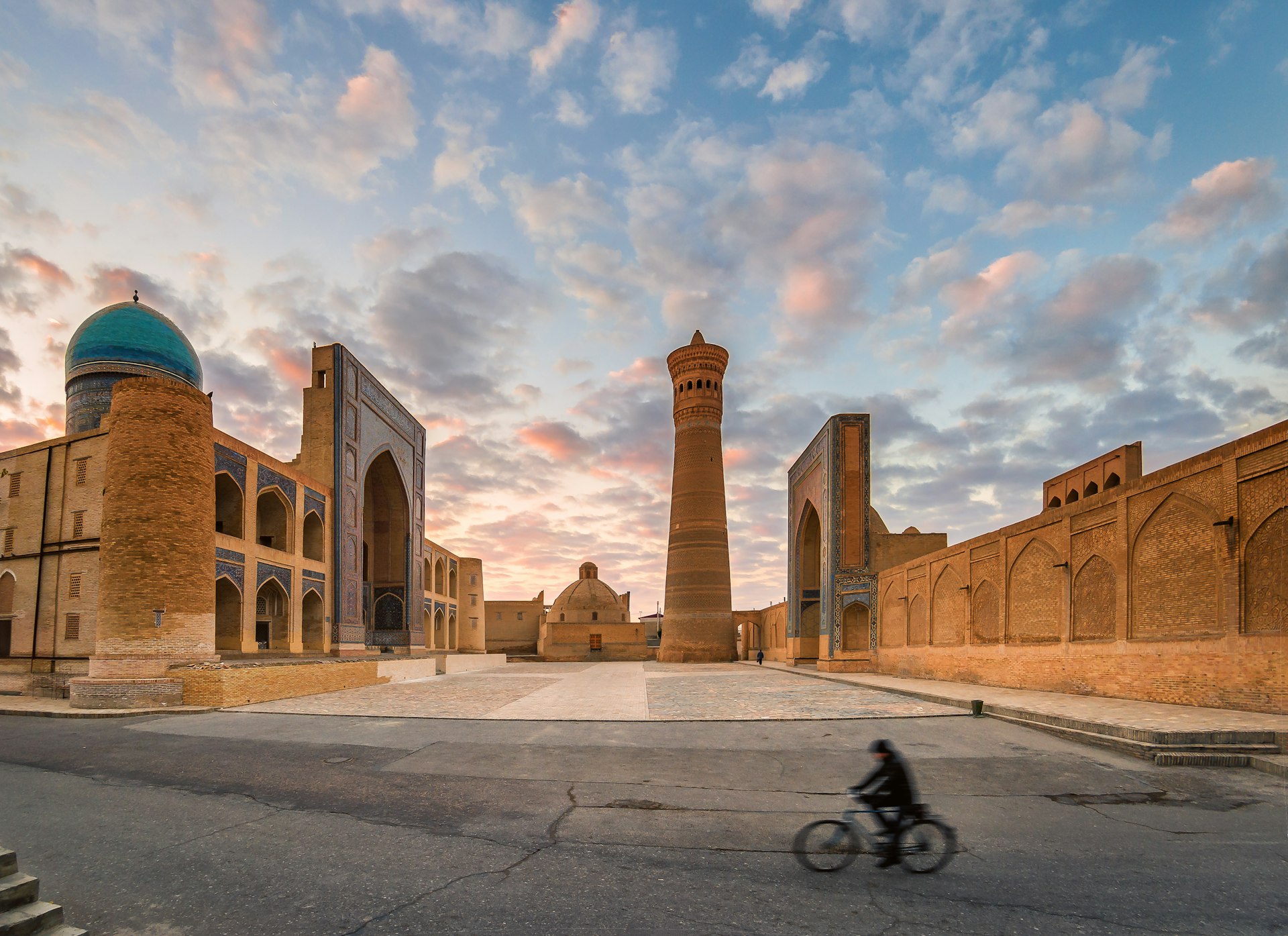 A cyclist passes by an epic square lined with ancient walls and a tall minaret