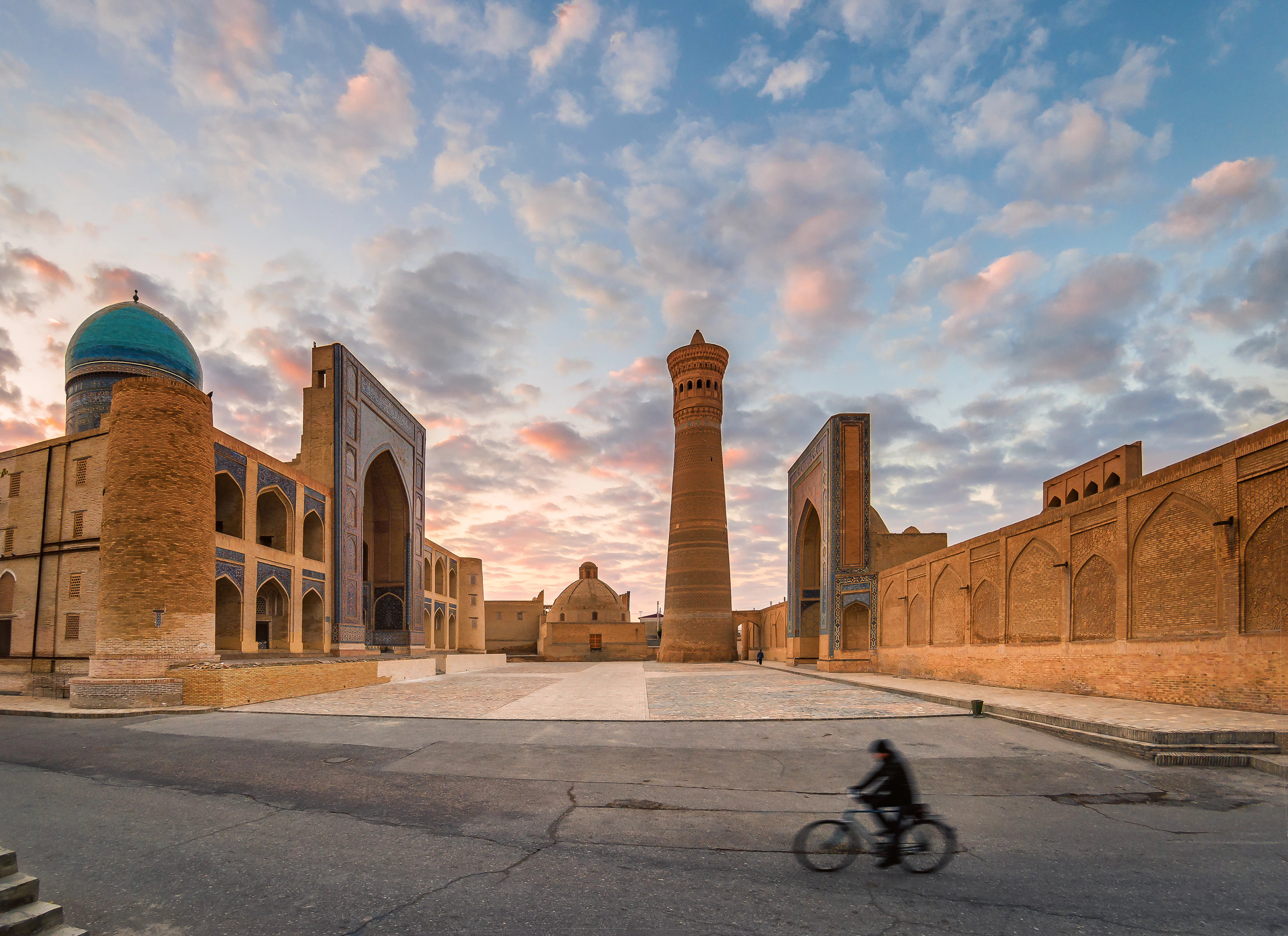 Мужчина, едущий на велосипеде мимо исламского памятника По-и-Каляна в Бухаре, Узбекистан