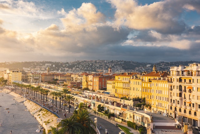 An aerial view of grand buildings and rows of palm trees fronting the beach on the Promenade des Anglais, Nice, Côte d’Azur, France