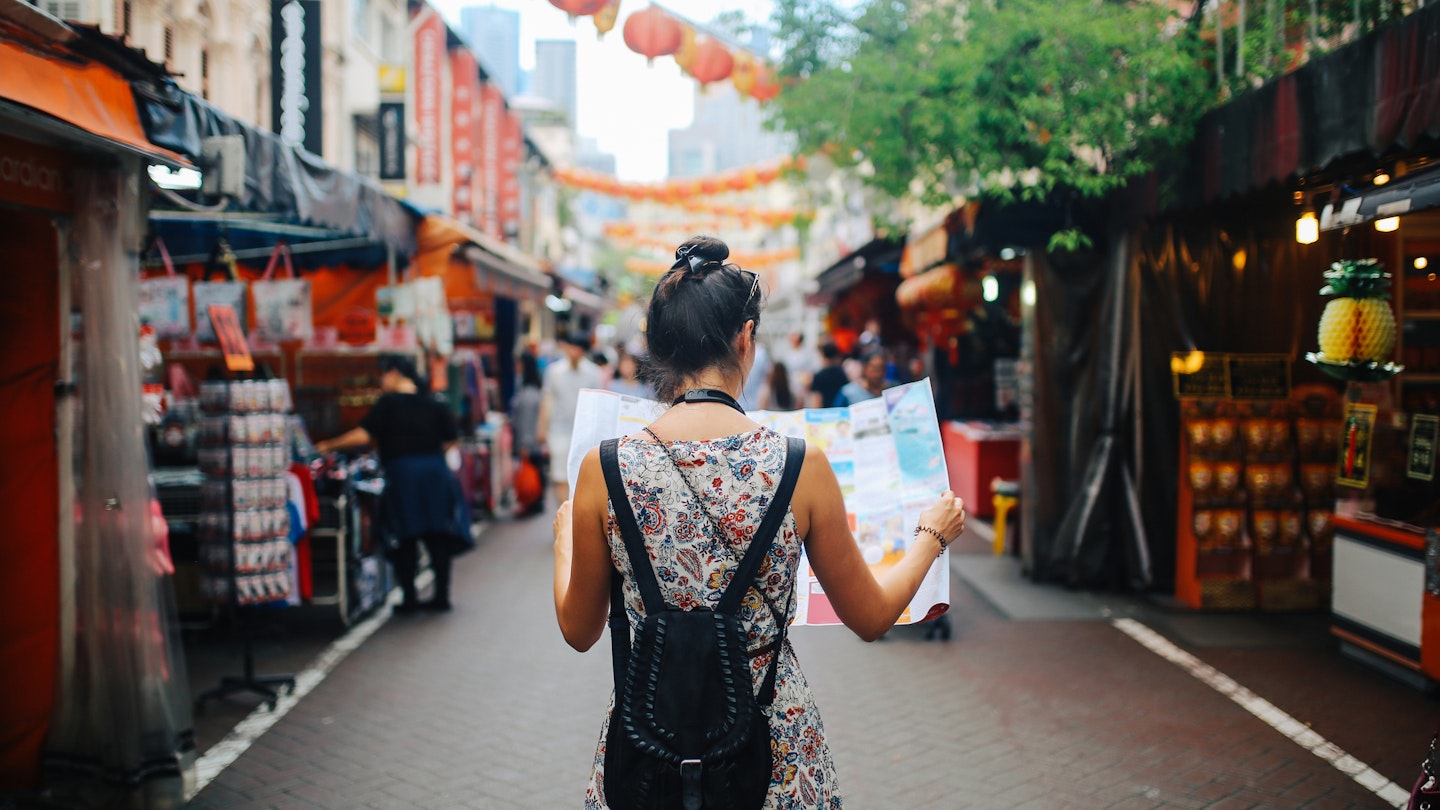 A young woman solo traveler checking a map in a Singapore street market