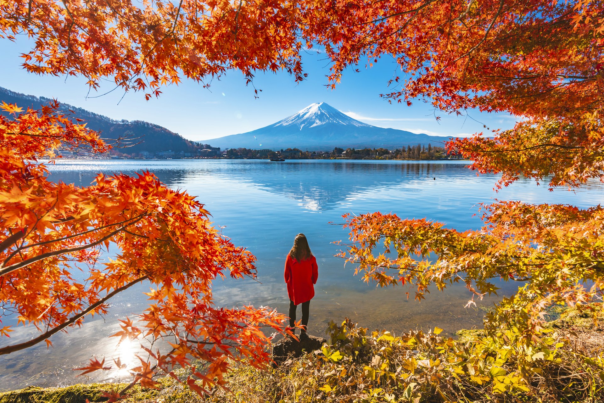 Woman framed by red maple leaves admiring Mount Fuji and Lake Kawaguchi in autumn, Japan