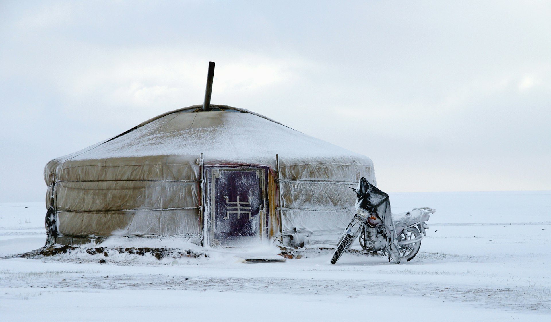 A motorcycle parked outside a round tent-link structure in a snow-covered landscape