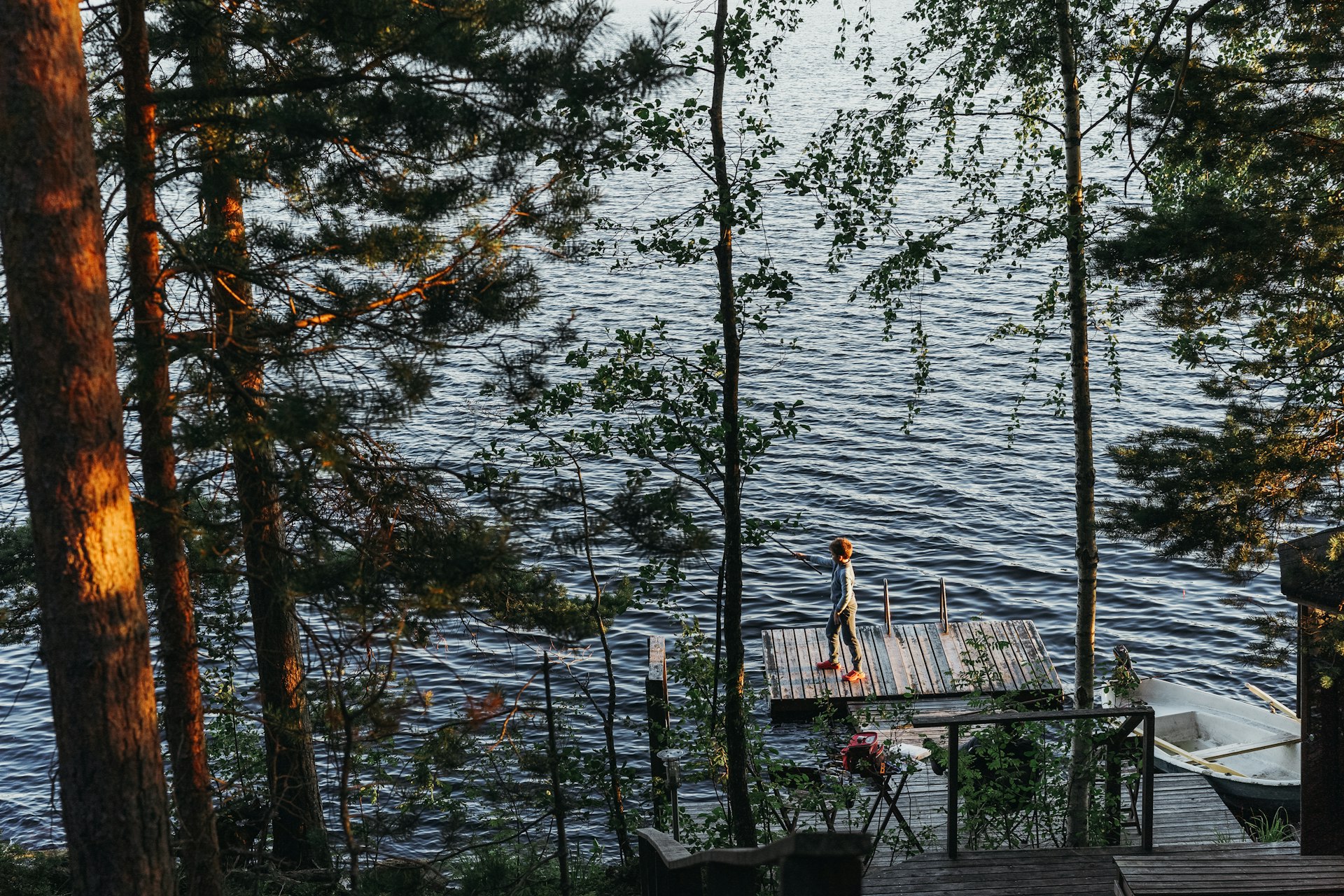 A young boy is fishing on a wooden pier by a lake in a forest, Finland