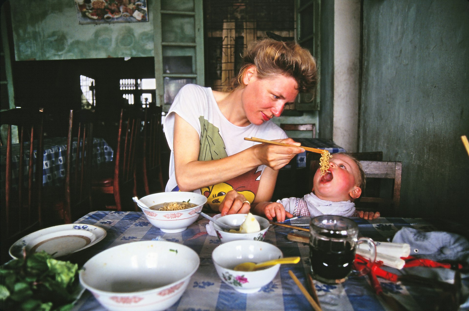 Mother feeding her two year old son some noodles from a bowl of noodles in Vietnam