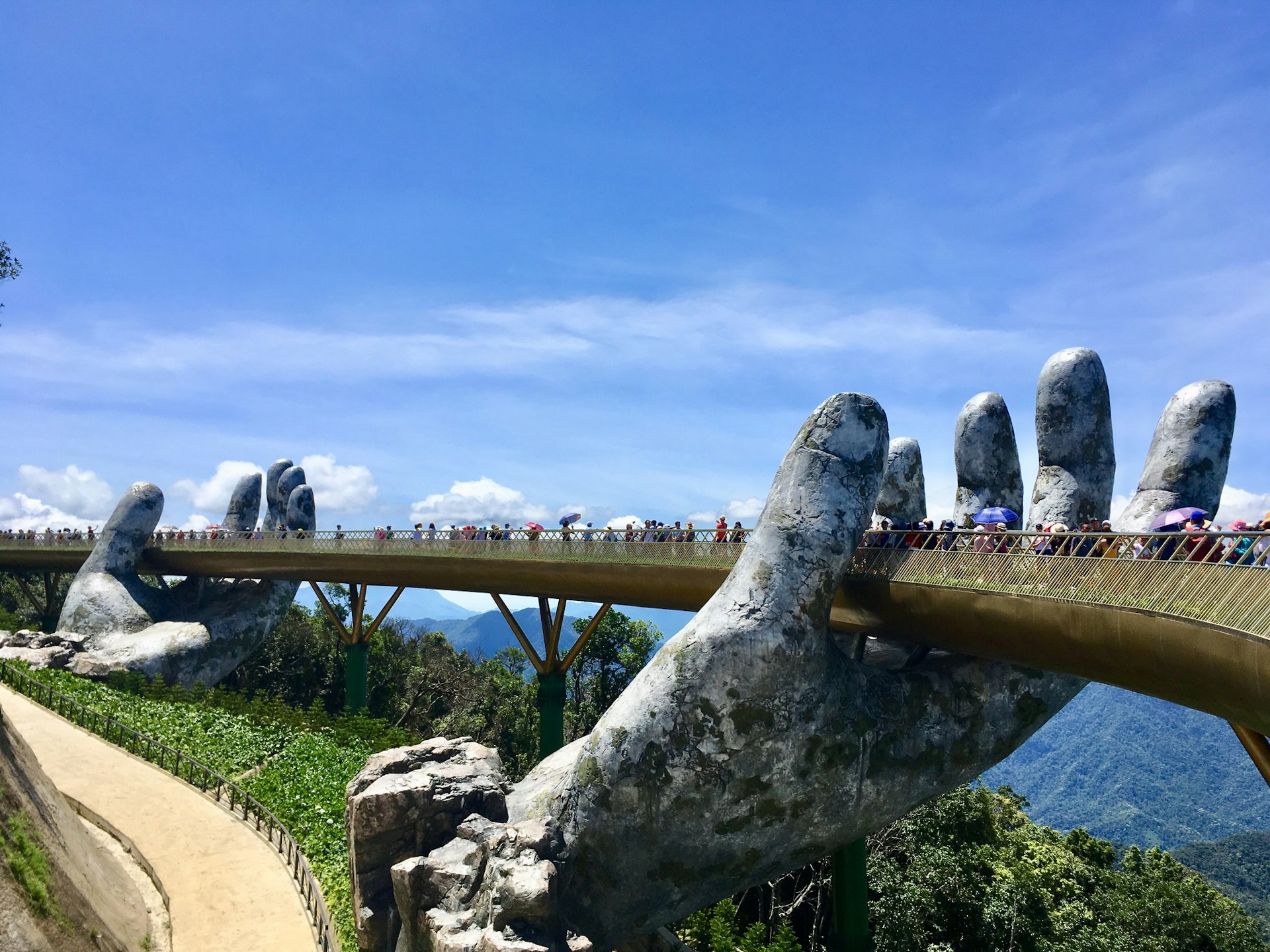 People walk along a bridge that is supported by two giant stone hands in a mountain resort