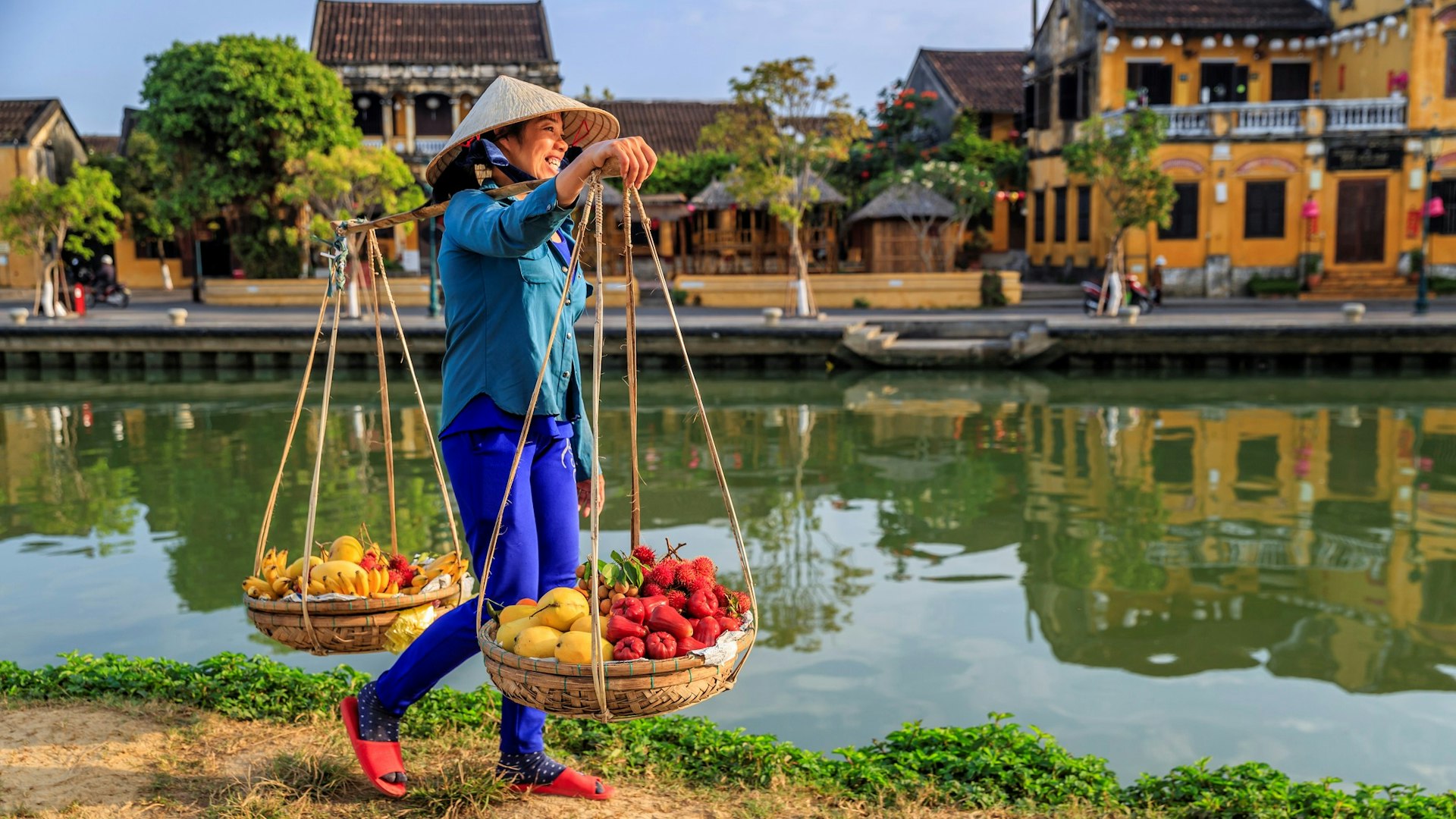 A woman carries baskets with fruits along a canal in the Old Town of Ha Noi, Vietnam