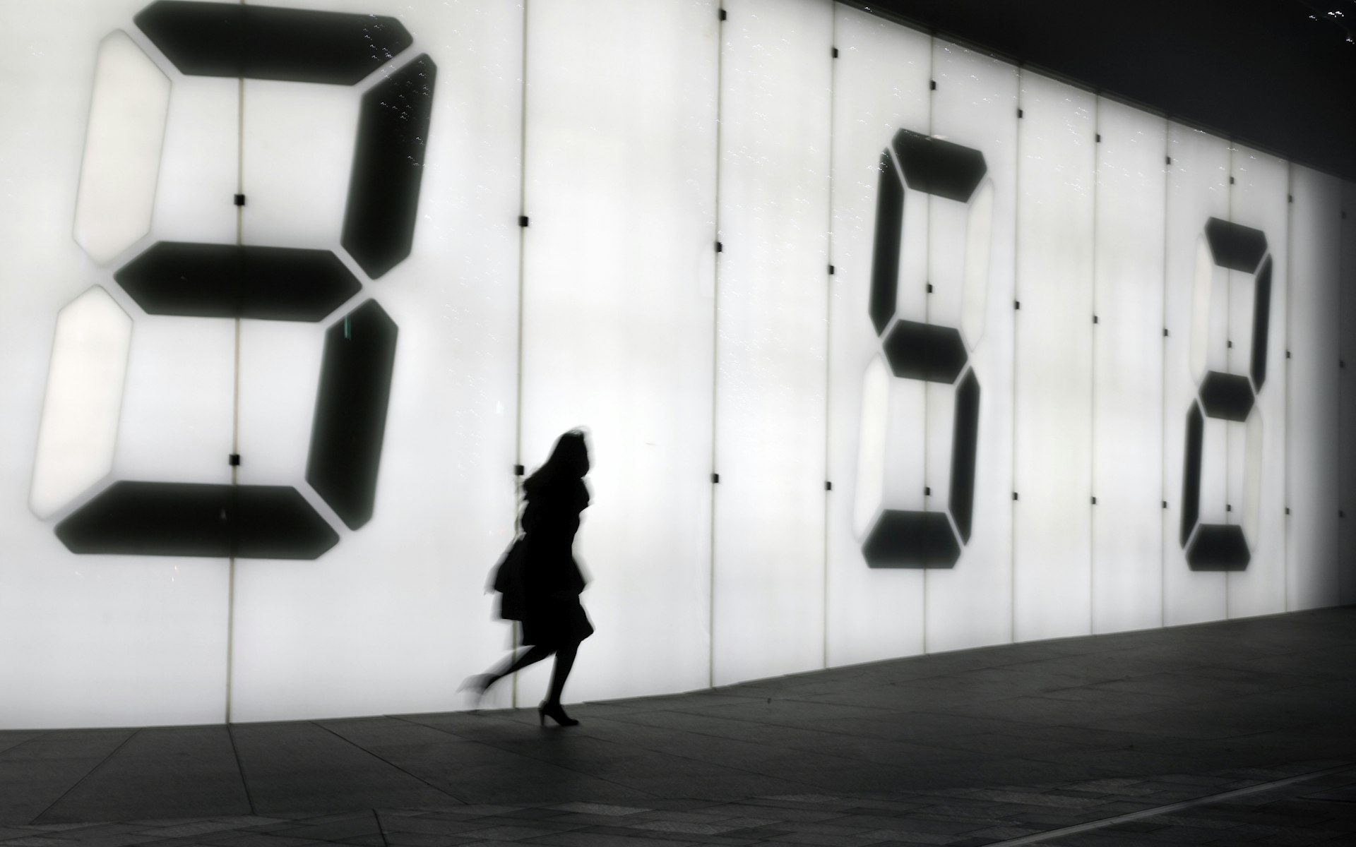 One female pedestrian walking alongside a digital clock display wall on the street at night in Roppongi, Tokyo, an area famous for its nightlife