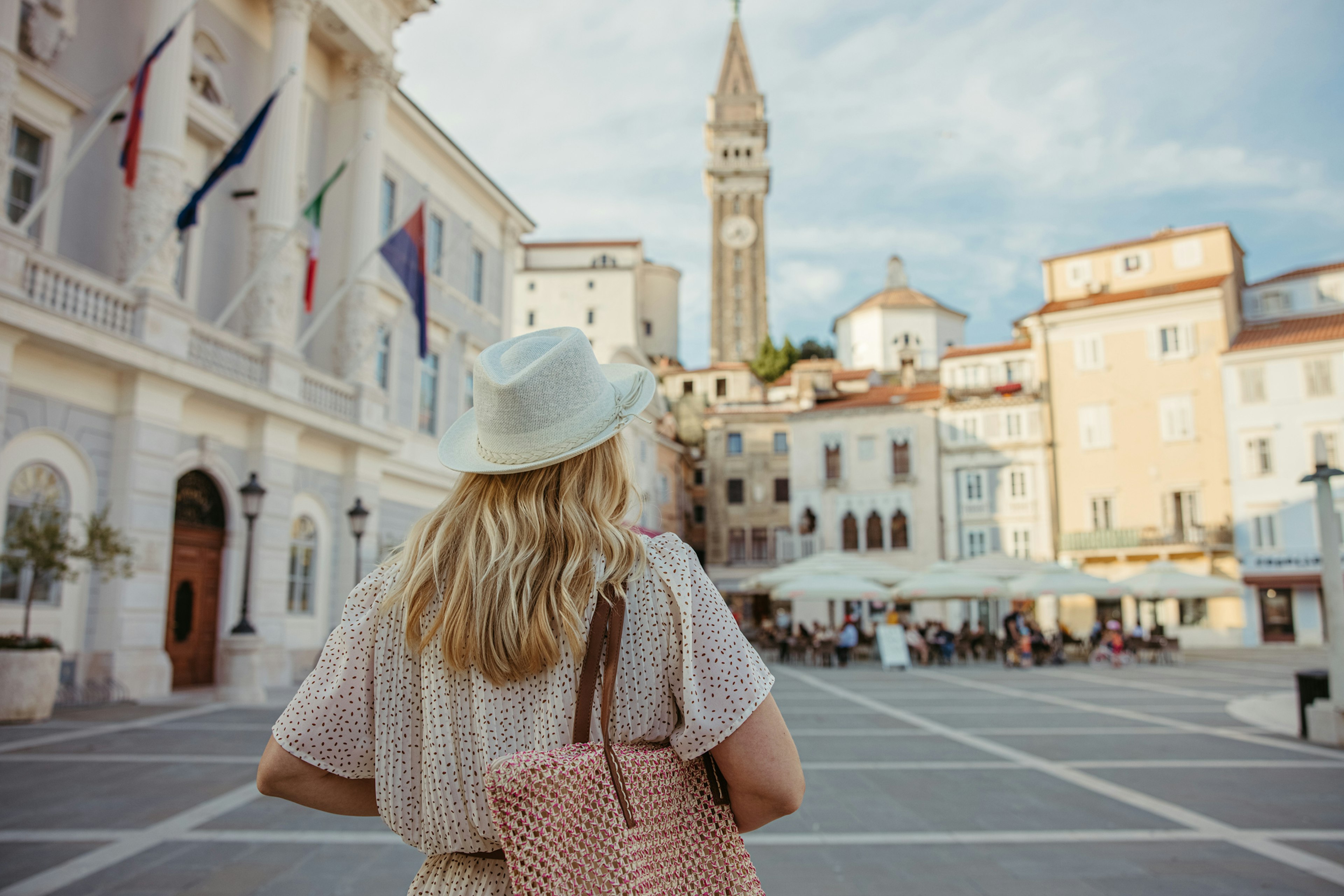 A woman walking through the center of Piran with the cathedral tower in the background