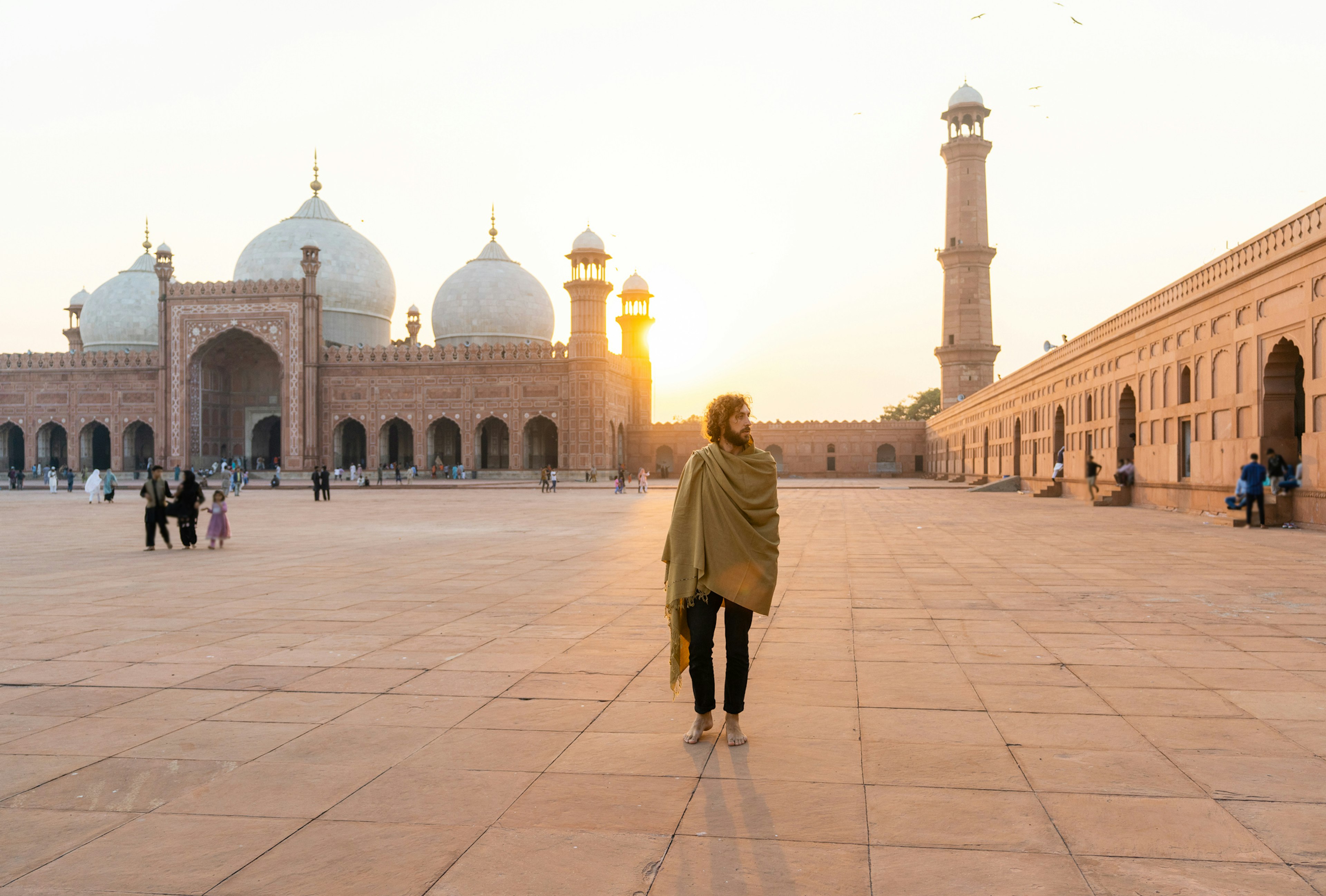 A man walks through the vast courtyard of a mosque complex as the sun sets