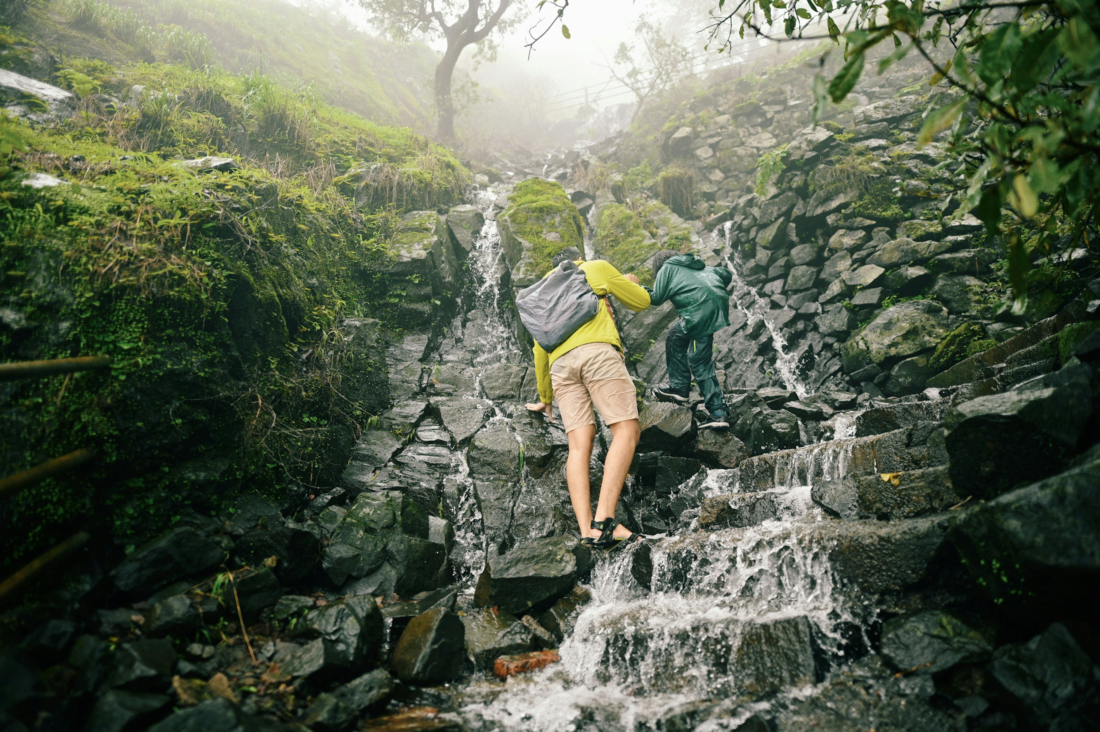 A dad and teenager help each other trekking up flooded rocks in India