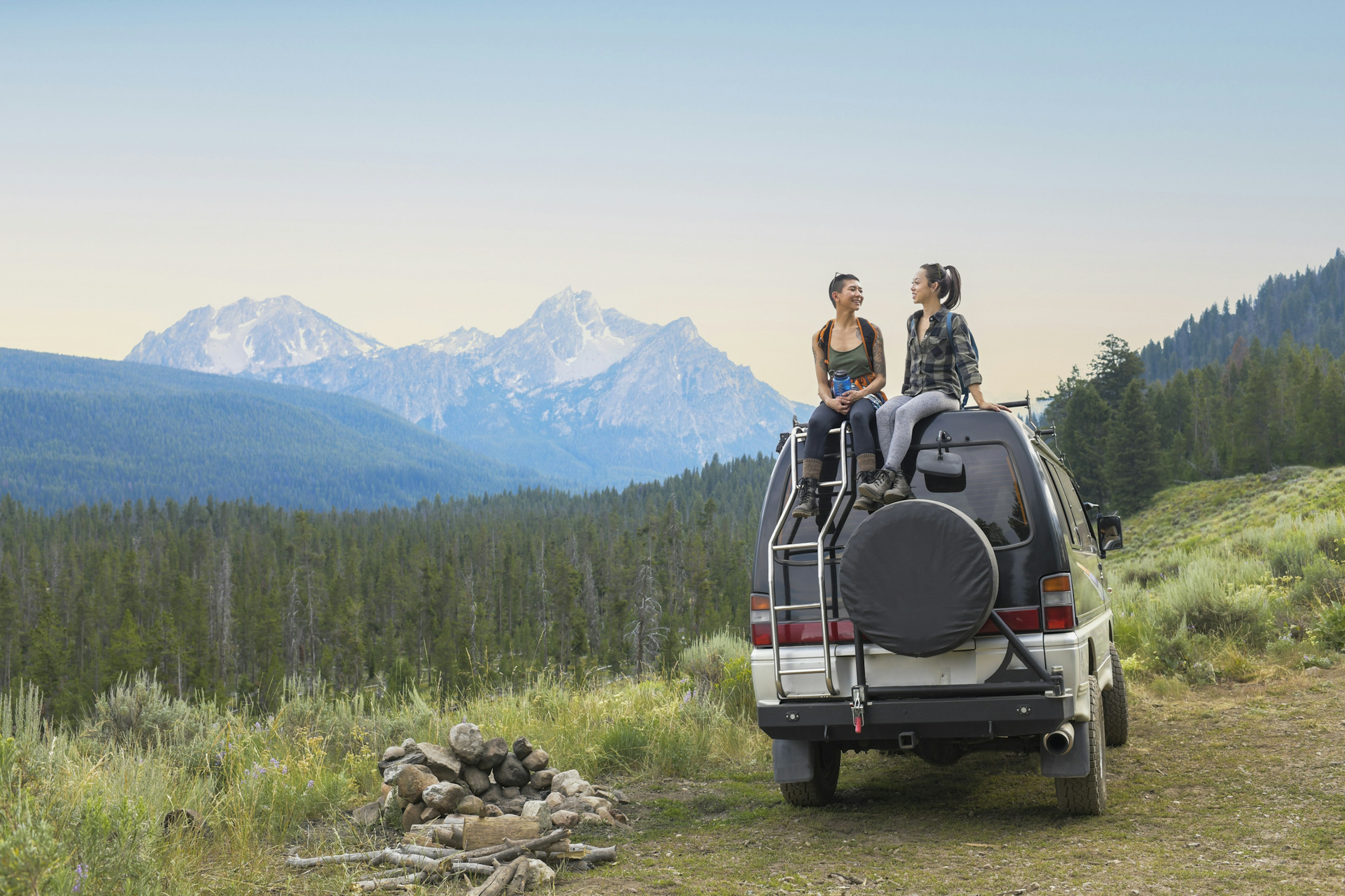 Two women sit on top of a four-wheel drive vehicle in a mountainous region