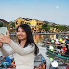 young woman standing on bridge in old town of Hoi An and looking together at smartphone at sunset hour
1453949562