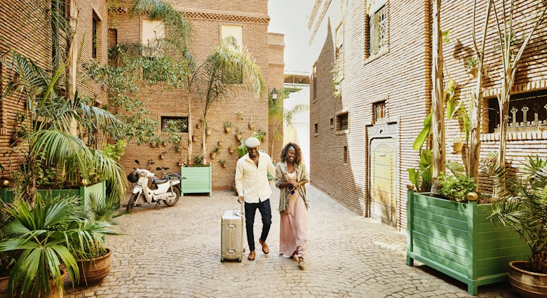 Wide shot of smiling and laughing couple arriving in hotel courtyard with rolling luggage while on vacation
1463514193
exotic travel
A smiling and laughing couple arriving in a hotel courtyard with luggage in Marrakech