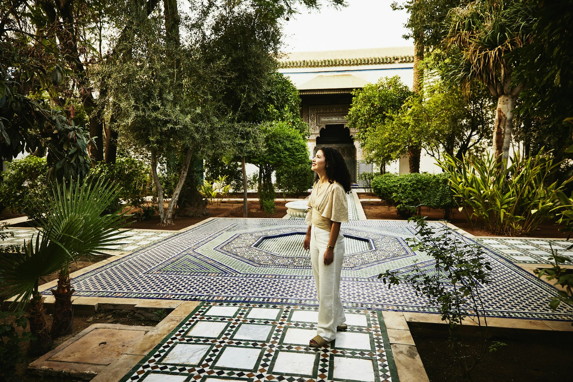 A woman smiles as she looks around a courtyard covered in intricate tiling 