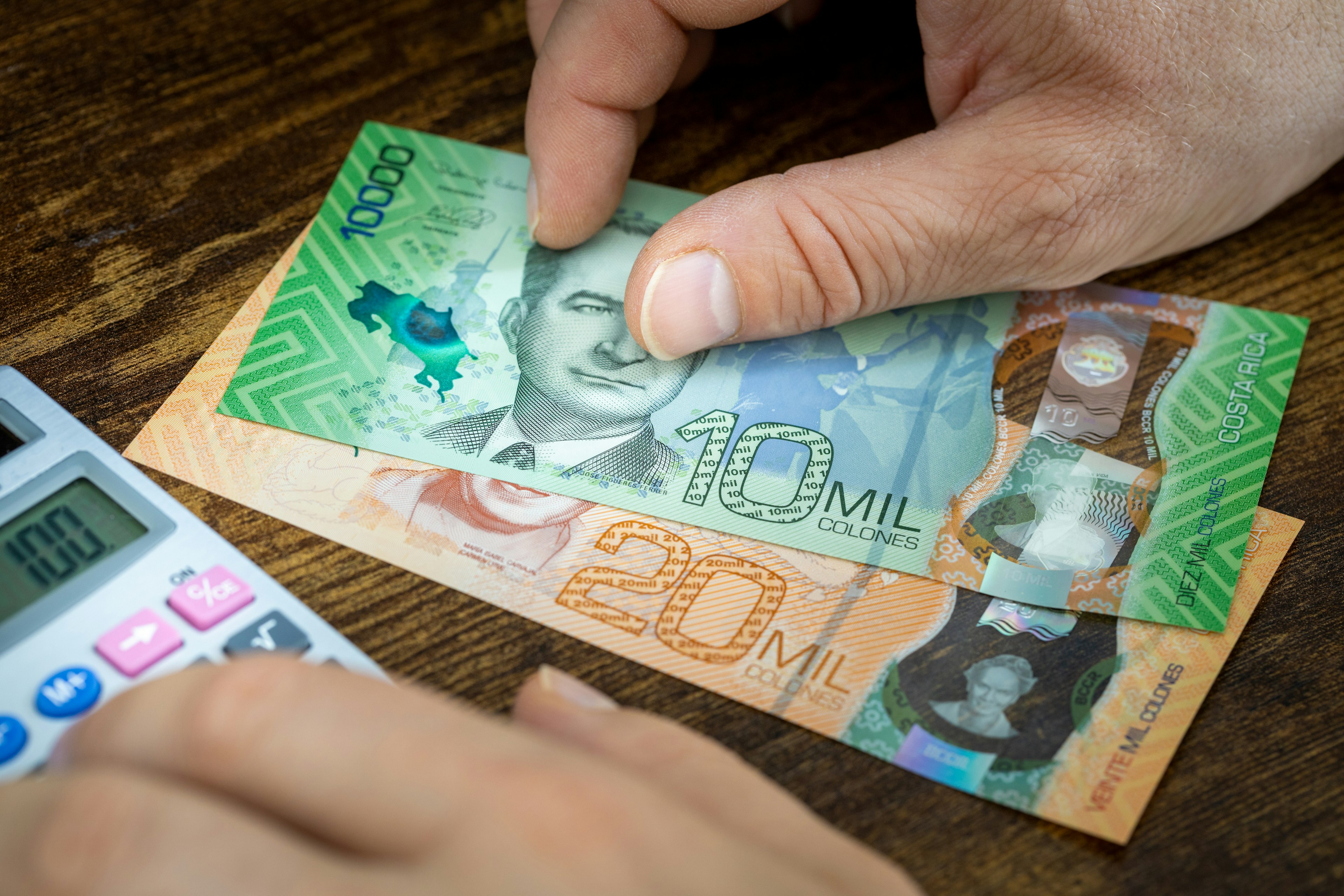 A man holding Costa Rican currency while using a calculator