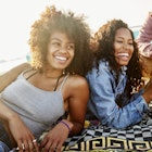 1496372996
Two Black women laughing with friends as they lay on a beach towel by the sea